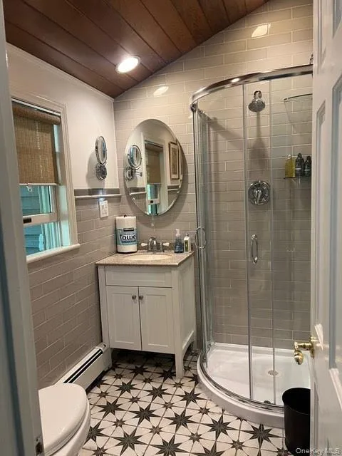 Full bathroom with tile walls, vanity, baseboard heating, a stall shower, and lofted ceiling Full bathroom with tile walls, vanity, baseboard heating, a stall shower, and lofted ceiling