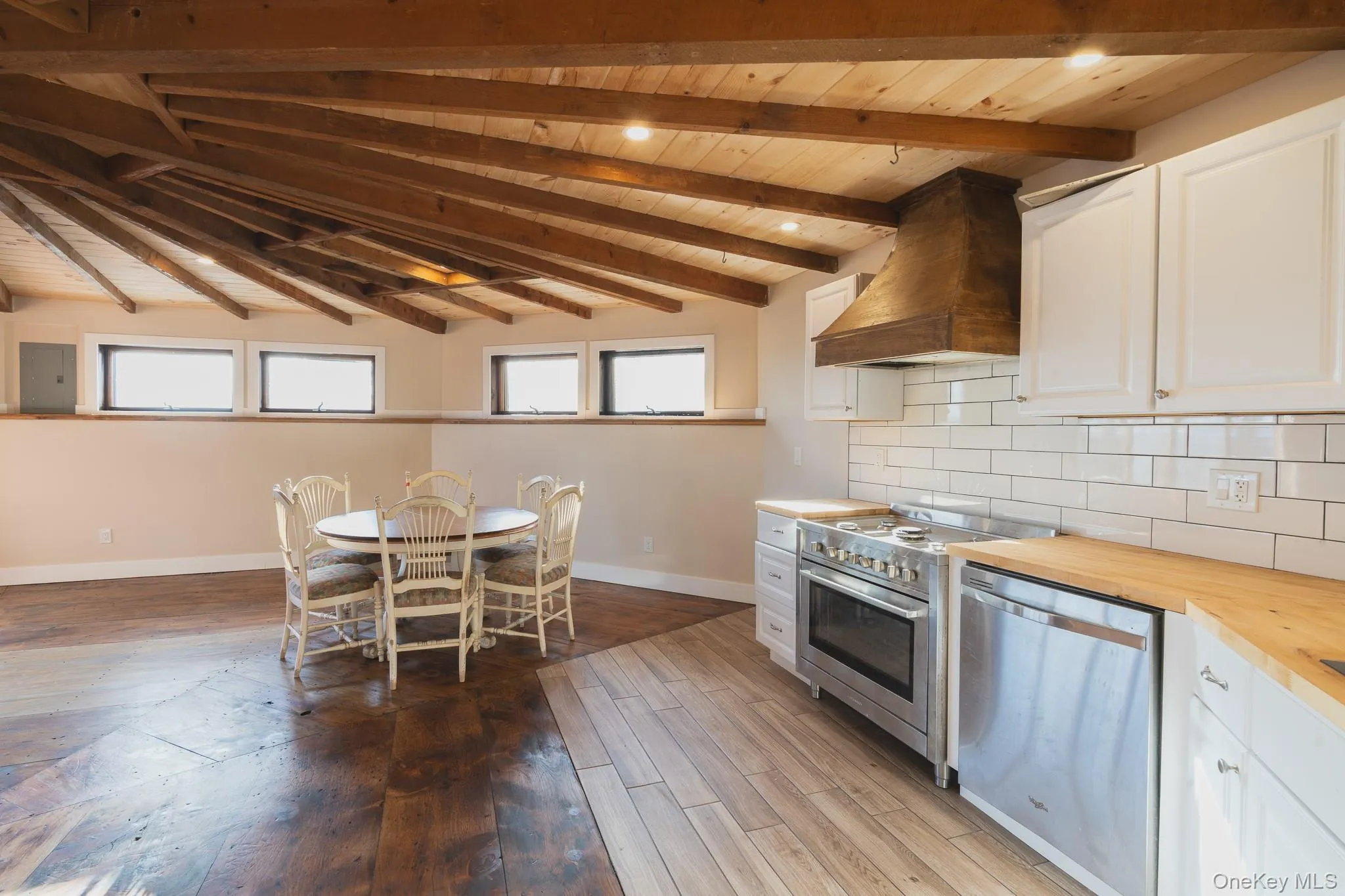 Kitchen featuring butcher block counters, custom exhaust hood, white cabinets, stainless steel appliances, and a wooden ceiling with exposed beams Kitchen featuring butcher block counters, custom exhaust hood, white cabinets, stainless steel appliances, and a wooden ceiling with exposed beams