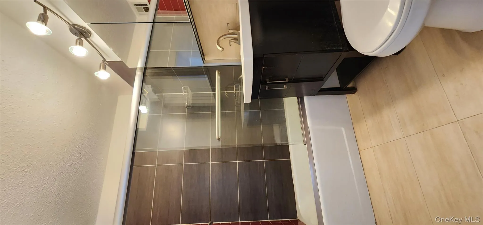 Full bath with bath / shower combo with glass door, light tile patterned floors, vanity, and a textured ceiling Full bath with bath / shower combo with glass door, light tile patterned floors, vanity, and a textured ceiling