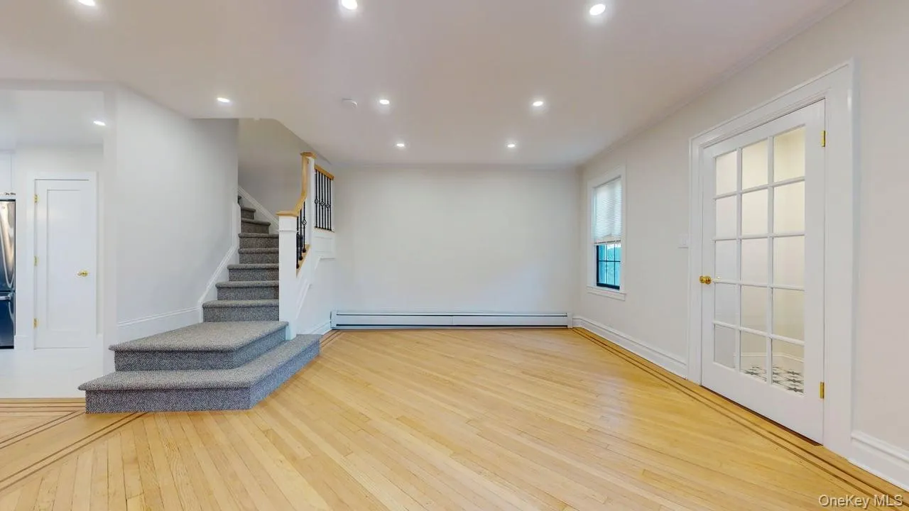 Unfurnished living room featuring recessed lighting, light wood-type flooring, stairs, and baseboard heating Unfurnished living room featuring recessed lighting, light wood-type flooring, stairs, and baseboard heating