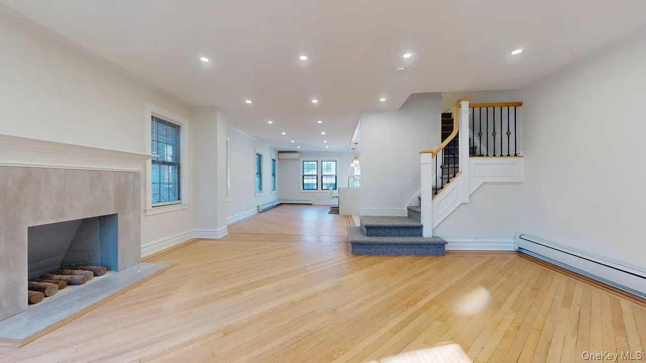 Unfurnished living room featuring recessed lighting, light wood-type flooring, stairs, a premium fireplace, and baseboard heating Unfurnished living room featuring recessed lighting, light wood-type flooring, stairs, a premium fireplace, and baseboard heating