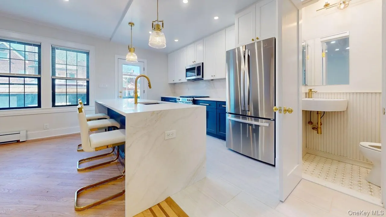Kitchen with stainless steel appliances, white cabinets, hanging light fixtures, a kitchen breakfast bar, and light stone counters Kitchen with stainless steel appliances, white cabinets, hanging light fixtures, a kitchen breakfast bar, and light stone counters
