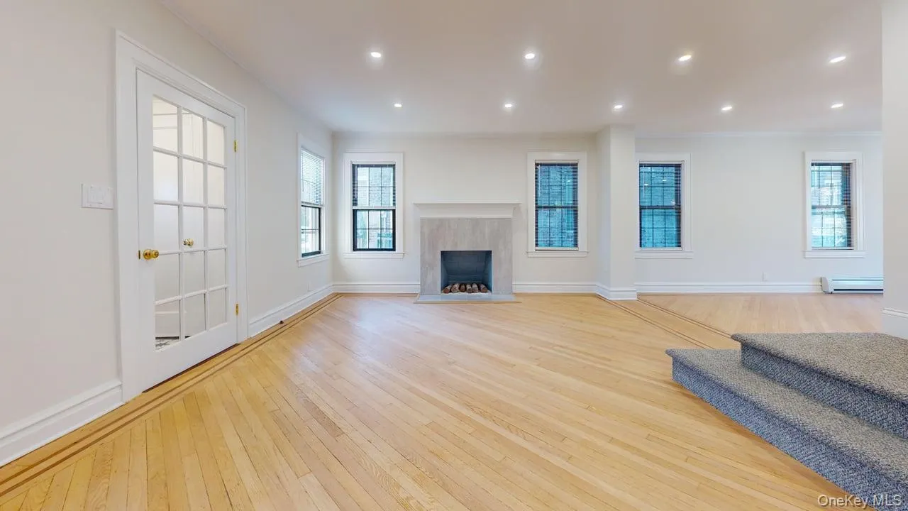 Unfurnished living room with a fireplace, light wood-type flooring, recessed lighting, baseboard heating, and ornamental molding Unfurnished living room with a fireplace, light wood-type flooring, recessed lighting, baseboard heating, and ornamental molding