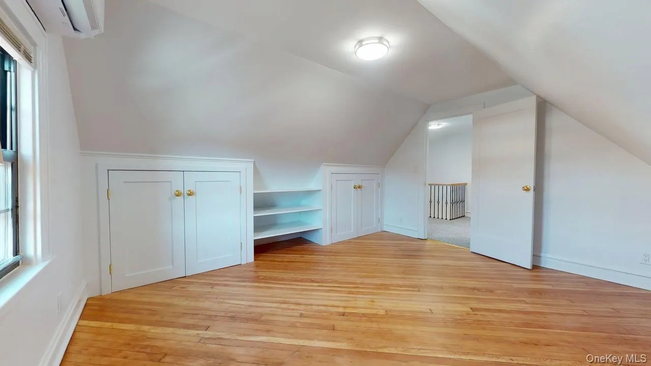 Additional living space with lofted ceiling, light wood-type flooring, a wall unit AC, and built in shelves Additional living space with lofted ceiling, light wood-type flooring, a wall unit AC, and built in shelves