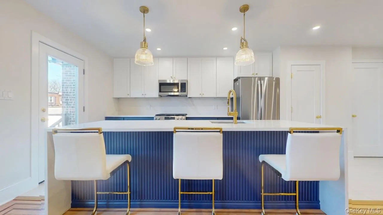 Kitchen featuring white cabinetry, stainless steel appliances, an island with sink, blue cabinets, and a breakfast bar area Kitchen featuring white cabinetry, stainless steel appliances, an island with sink, blue cabinets, and a breakfast bar area