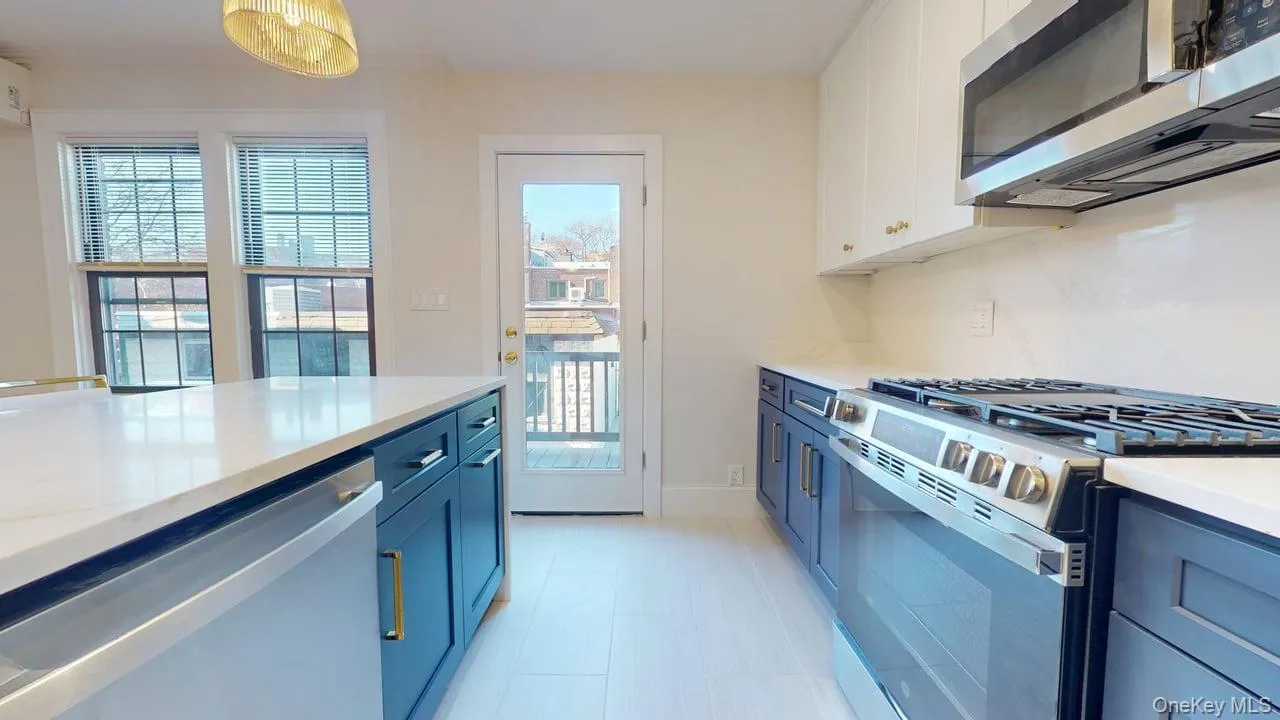 Kitchen featuring appliances with stainless steel finishes, light stone counters, white cabinets, blue cabinets, and hanging light fixtures Kitchen featuring appliances with stainless steel finishes, light stone counters, white cabinets, blue cabinets, and hanging light fixtures