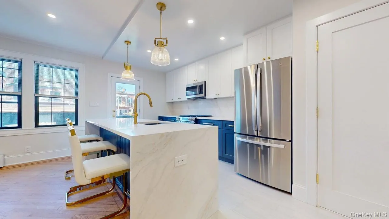 Kitchen with white cabinetry, stainless steel appliances, hanging light fixtures, a kitchen breakfast bar, and light wood-type flooring Kitchen with white cabinetry, stainless steel appliances, hanging light fixtures, a kitchen breakfast bar, and light wood-type flooring