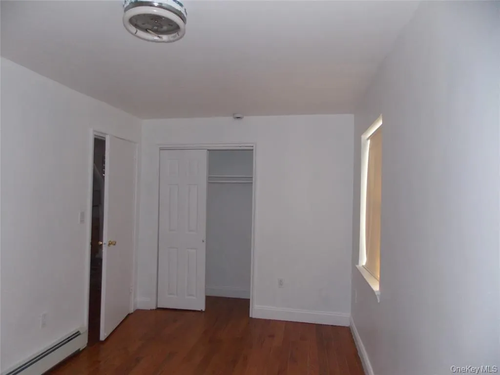 Unfurnished bedroom with a baseboard radiator, dark wood finished floors, and a closet Unfurnished bedroom with a baseboard radiator, dark wood finished floors, and a closet