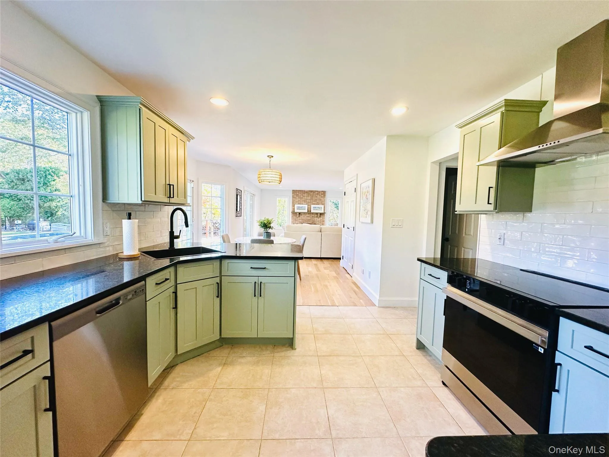 Kitchen with decorative backsplash, green cabinetry, appliances with stainless steel finishes, wall chimney exhaust hood, and a peninsula Kitchen with decorative backsplash, green cabinetry, appliances with stainless steel finishes, wall chimney exhaust hood, and a peninsula