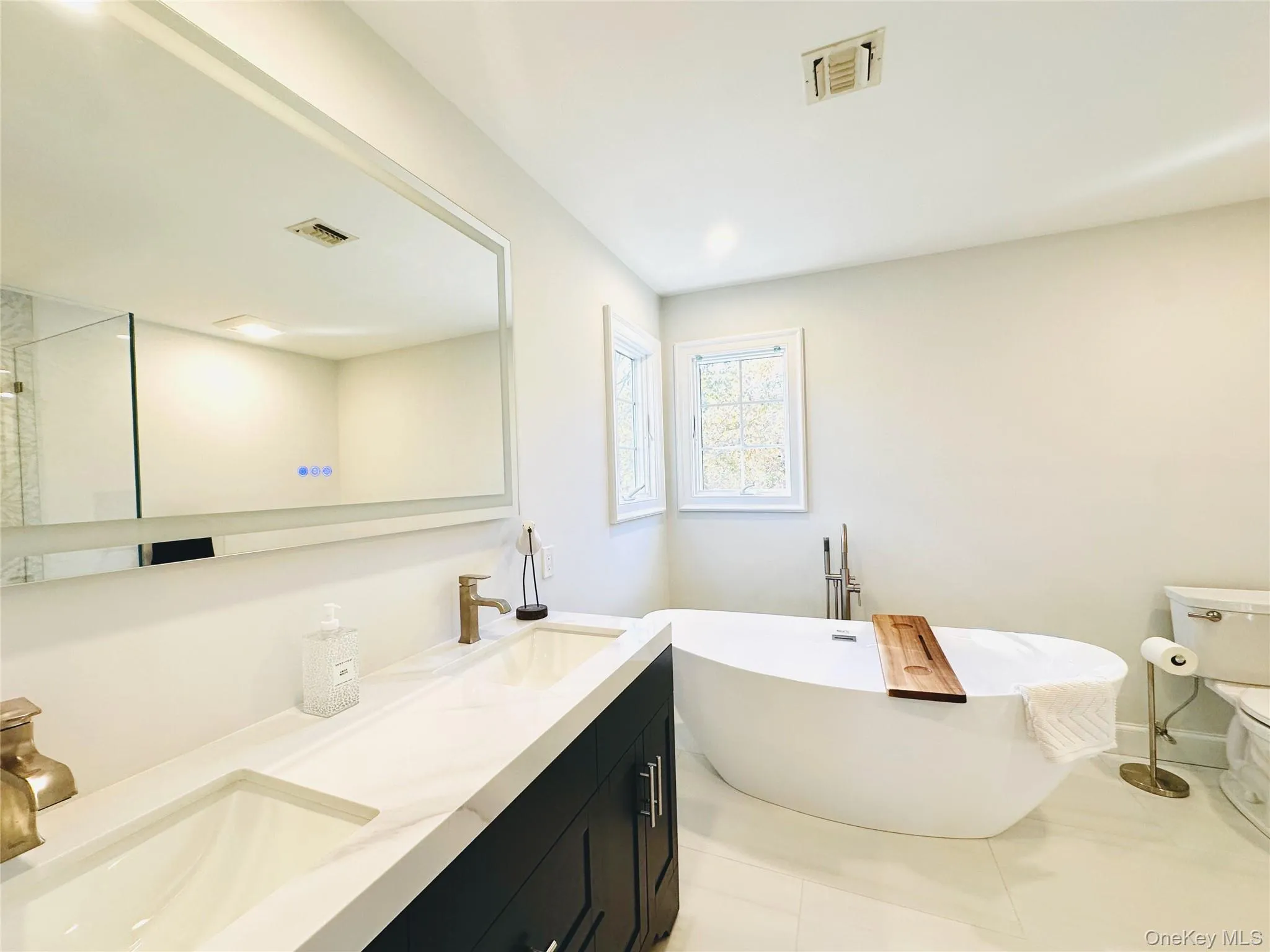 Bathroom featuring a freestanding bath, double vanity, and light tile patterned floors Bathroom featuring a freestanding bath, double vanity, and light tile patterned floors