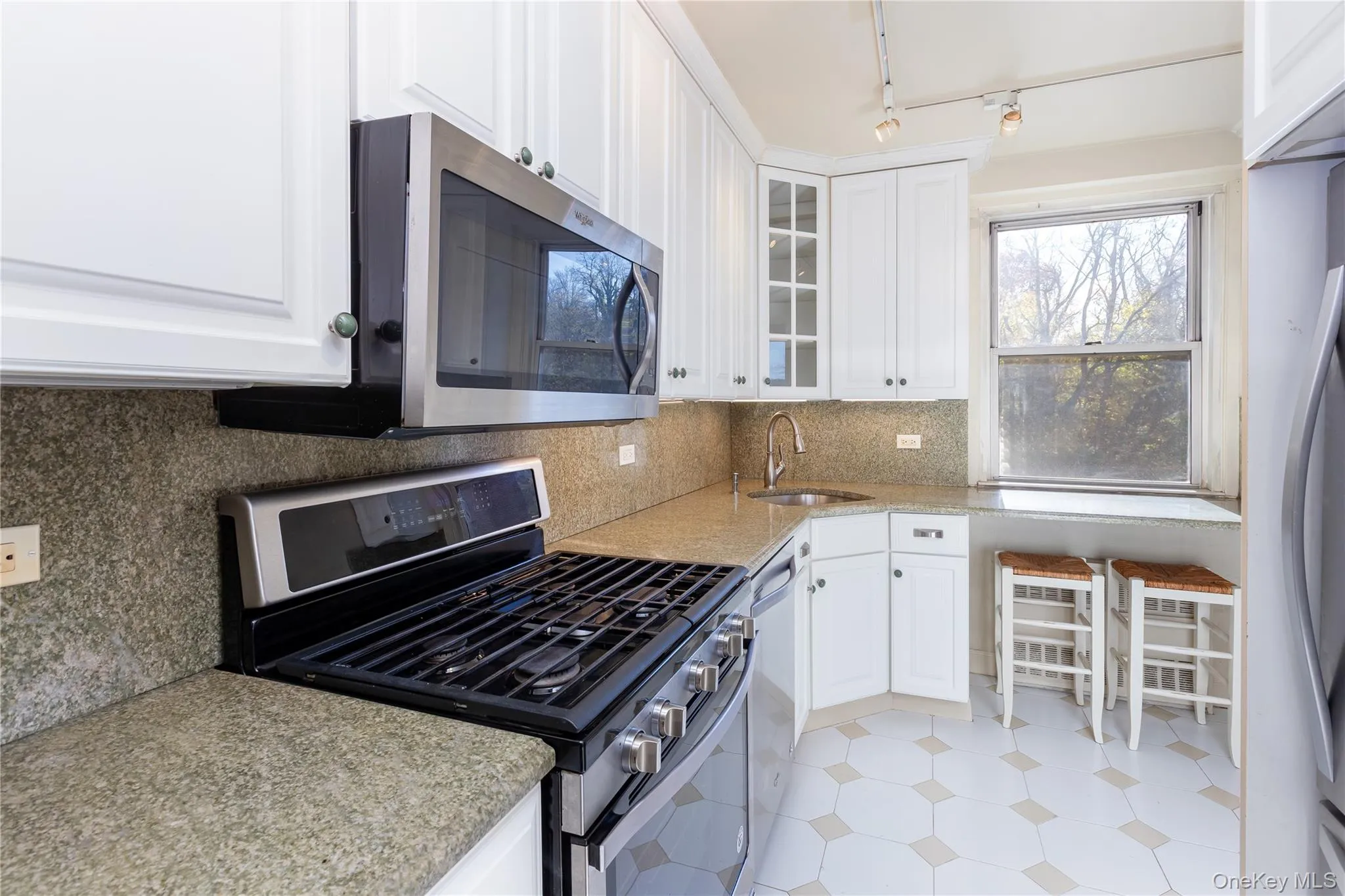 Kitchen featuring stainless steel appliances, white cabinets, decorative backsplash, light stone counters, and glass insert cabinets Kitchen featuring stainless steel appliances, white cabinets, decorative backsplash, light stone counters, and glass insert cabinets