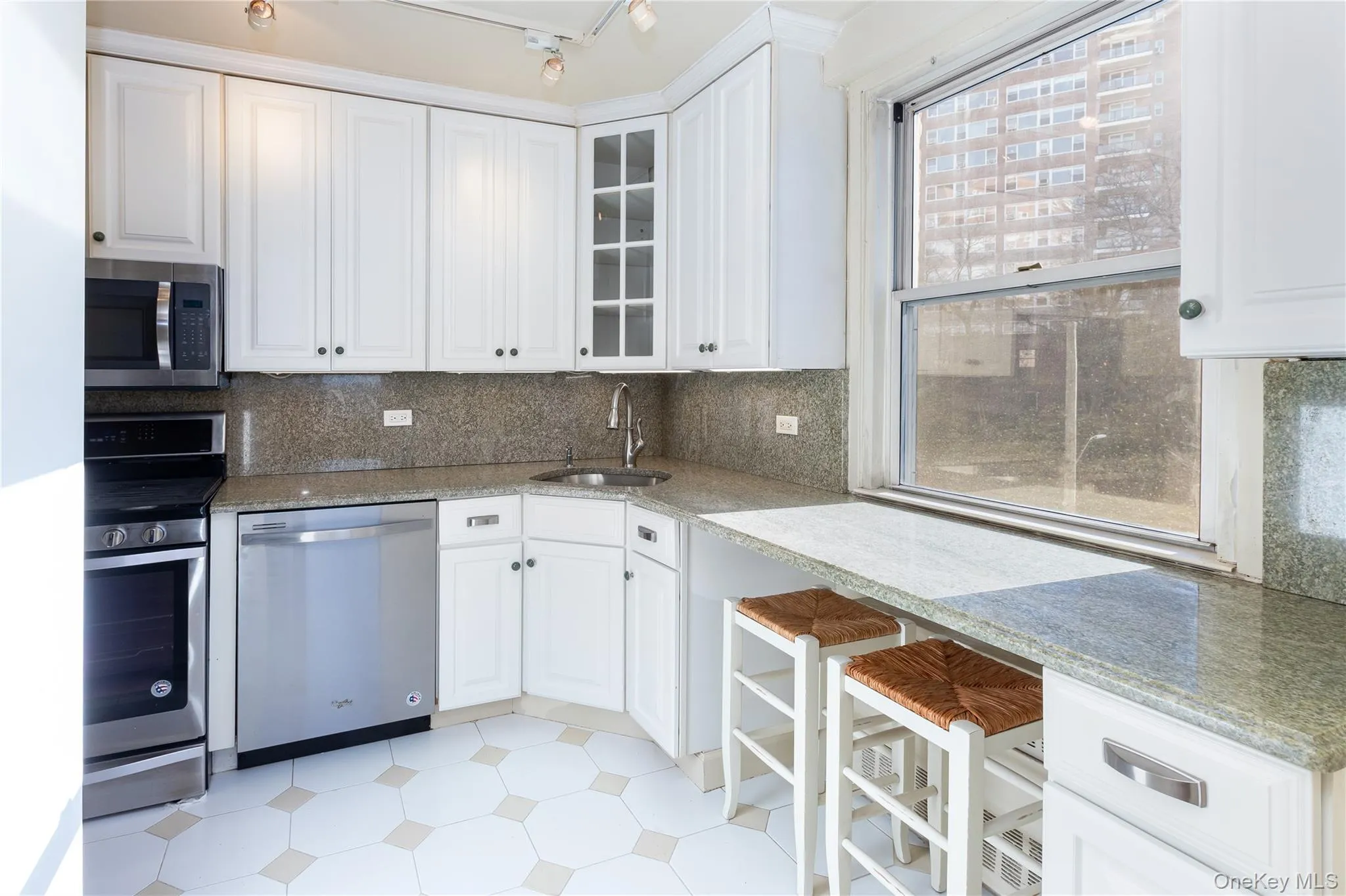 Kitchen featuring stainless steel appliances, white cabinets, light stone counters, and glass insert cabinets Kitchen featuring stainless steel appliances, white cabinets, light stone counters, and glass insert cabinets