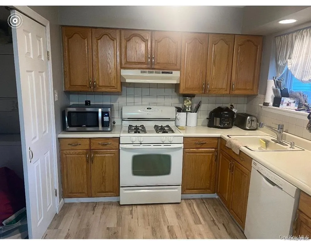 Kitchen with white appliances, brown cabinetry, light countertops, and light wood-style floors Kitchen with white appliances, brown cabinetry, light countertops, and light wood-style floors