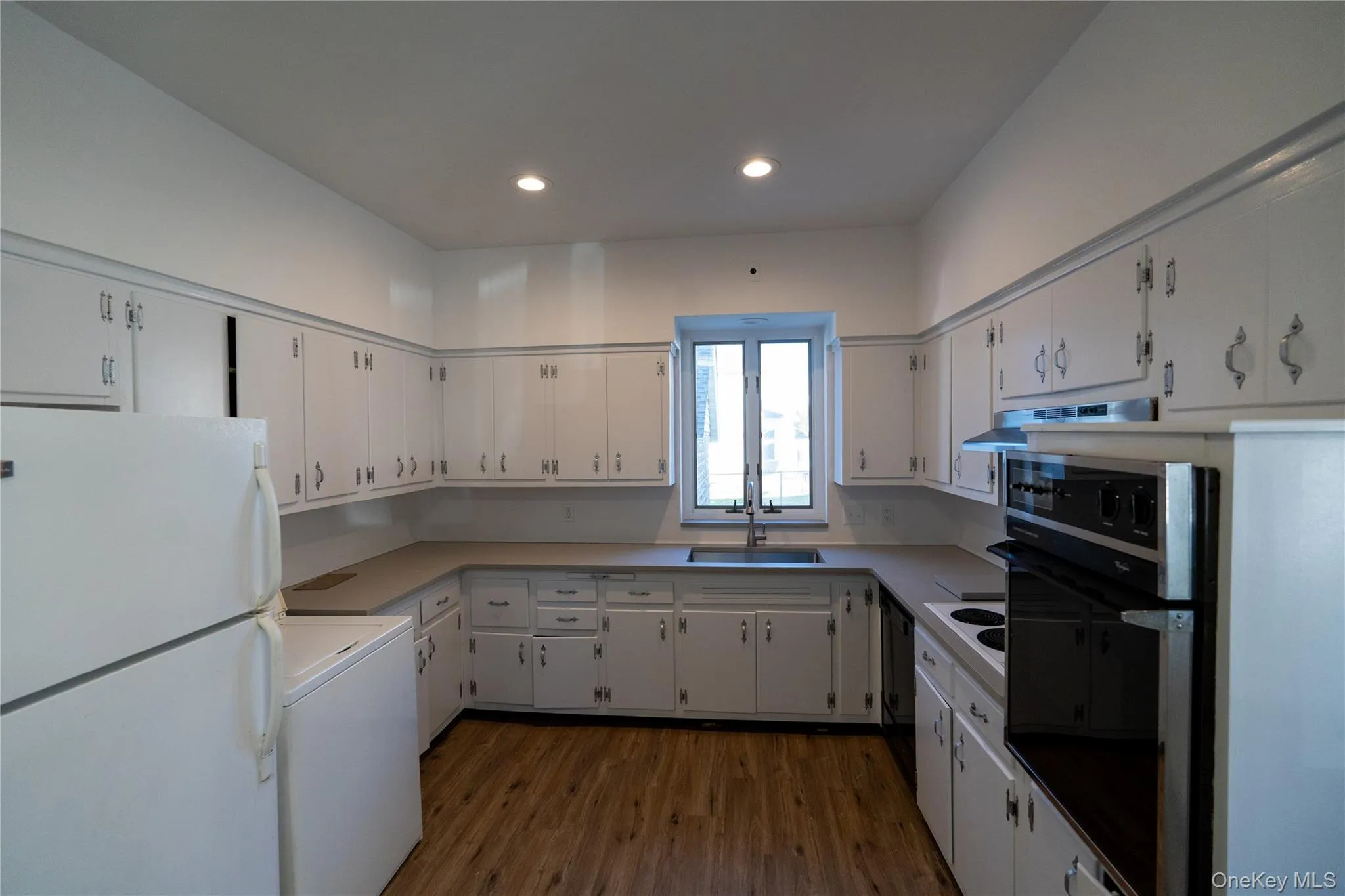 Kitchen featuring black appliances, white cabinetry, dark wood-style floors, light countertops, and recessed lighting Kitchen featuring black appliances, white cabinetry, dark wood-style floors, light countertops, and recessed lighting