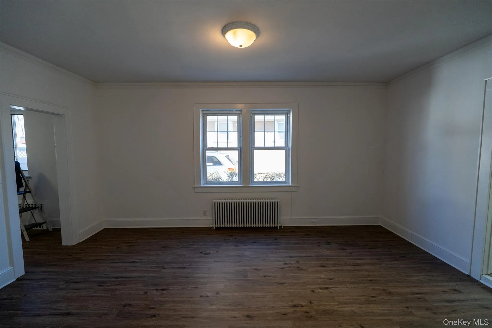 Unfurnished room featuring radiator, dark wood-type flooring, and crown molding Unfurnished room featuring radiator, dark wood-type flooring, and crown molding