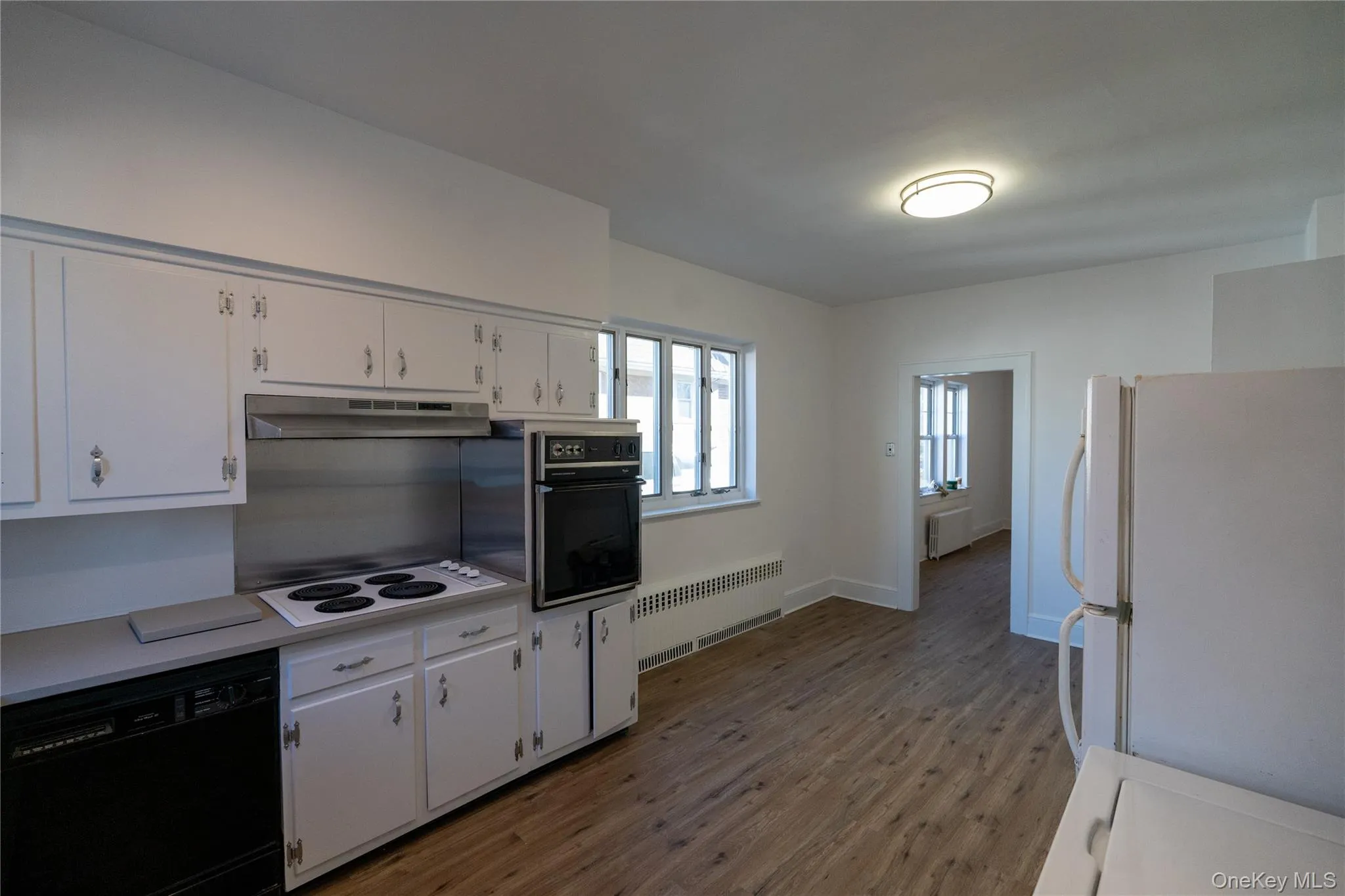 Kitchen with black appliances, light countertops, radiator heating unit, light wood-type flooring, and white cabinets Kitchen with black appliances, light countertops, radiator heating unit, light wood-type flooring, and white cabinets