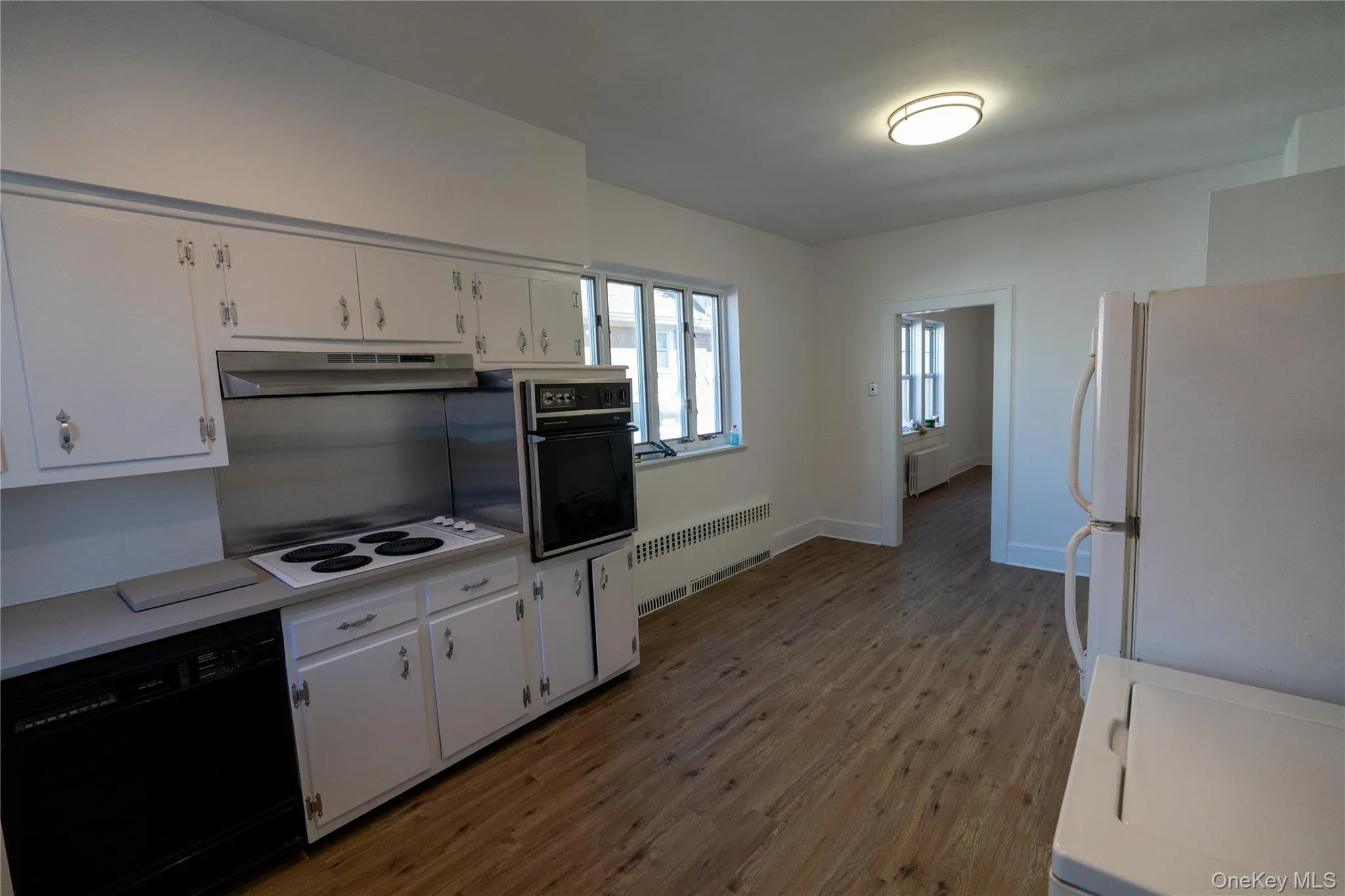 Kitchen with black appliances, light countertops, light wood-style floors, radiator, and white cabinetry Kitchen with black appliances, light countertops, light wood-style floors, radiator, and white cabinetry