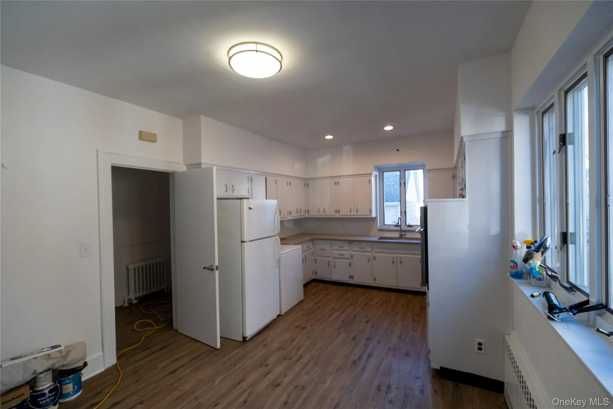Kitchen featuring freestanding refrigerator, white cabinetry, dark wood-style floors, light countertops, and radiator Kitchen featuring freestanding refrigerator, white cabinetry, dark wood-style floors, light countertops, and radiator