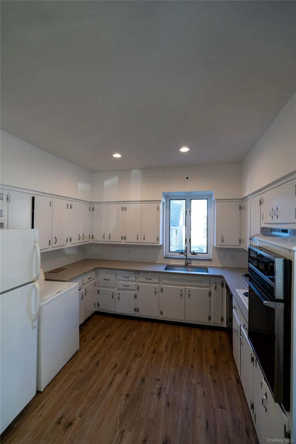 Kitchen with white cabinets, freestanding refrigerator, light countertops, dark wood finished floors, and recessed lighting Kitchen with white cabinets, freestanding refrigerator, light countertops, dark wood finished floors, and recessed lighting