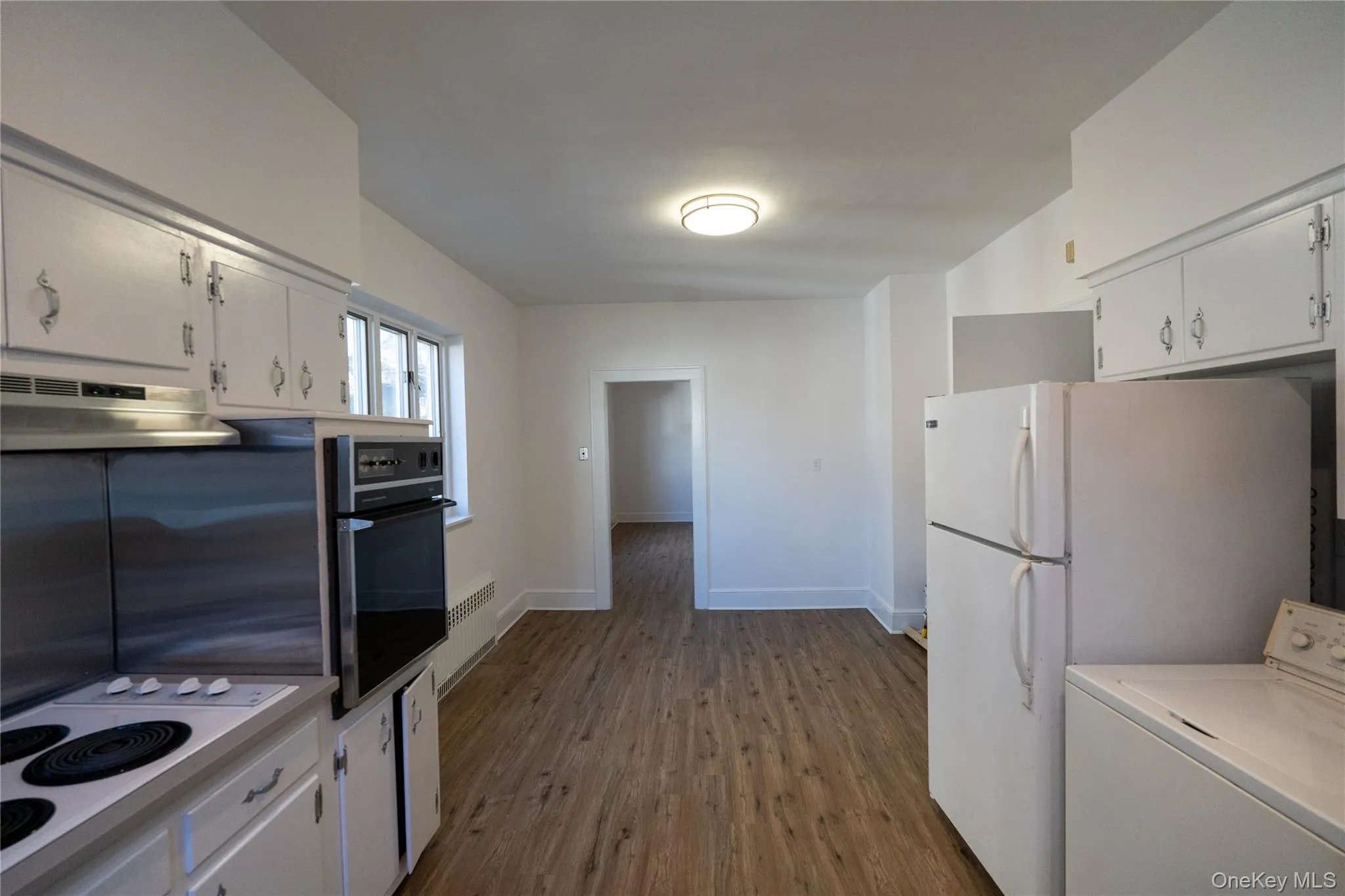 Kitchen featuring washer / dryer, dark wood-style floors, white appliances, white cabinets, and under cabinet range hood Kitchen featuring washer / dryer, dark wood-style floors, white appliances, white cabinets, and under cabinet range hood