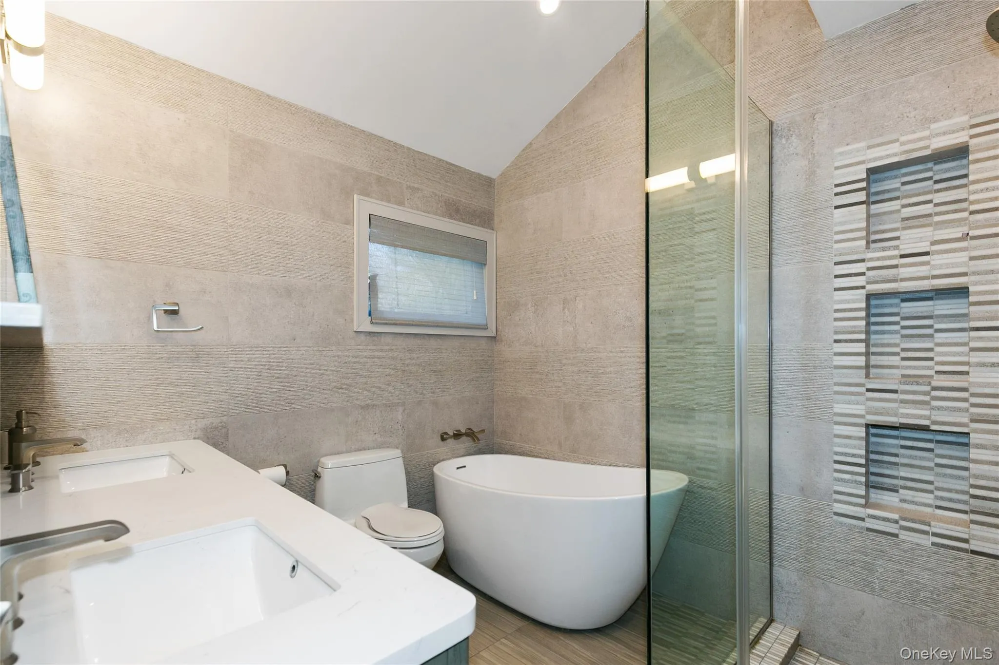 Bathroom featuring tile walls, double vanity, a soaking tub, lofted ceiling, and a walk in shower Bathroom featuring tile walls, double vanity, a soaking tub, lofted ceiling, and a walk in shower