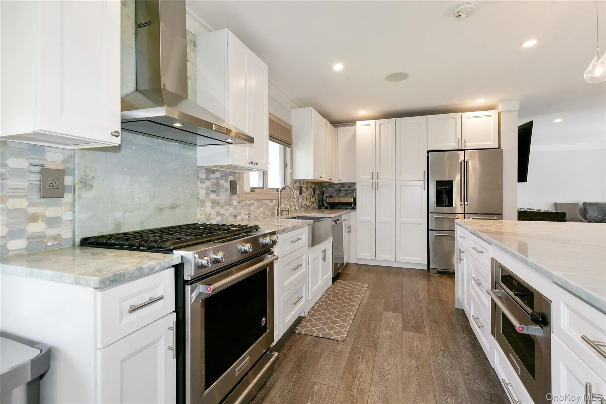 Kitchen with wall chimney range hood, appliances with stainless steel finishes, white cabinetry, dark wood finished floors, and recessed lighting Kitchen with wall chimney range hood, appliances with stainless steel finishes, white cabinetry, dark wood finished floors, and recessed lighting
