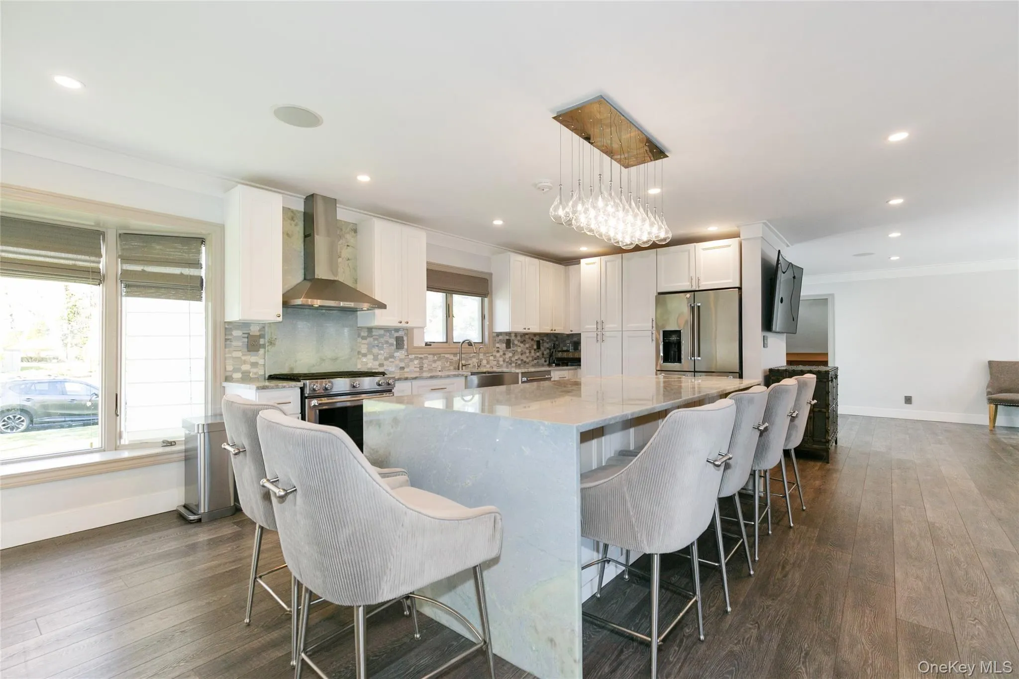 Kitchen with a breakfast bar, ornamental molding, light stone countertops, white cabinetry, and wall chimney range hood Kitchen with a breakfast bar, ornamental molding, light stone countertops, white cabinetry, and wall chimney range hood