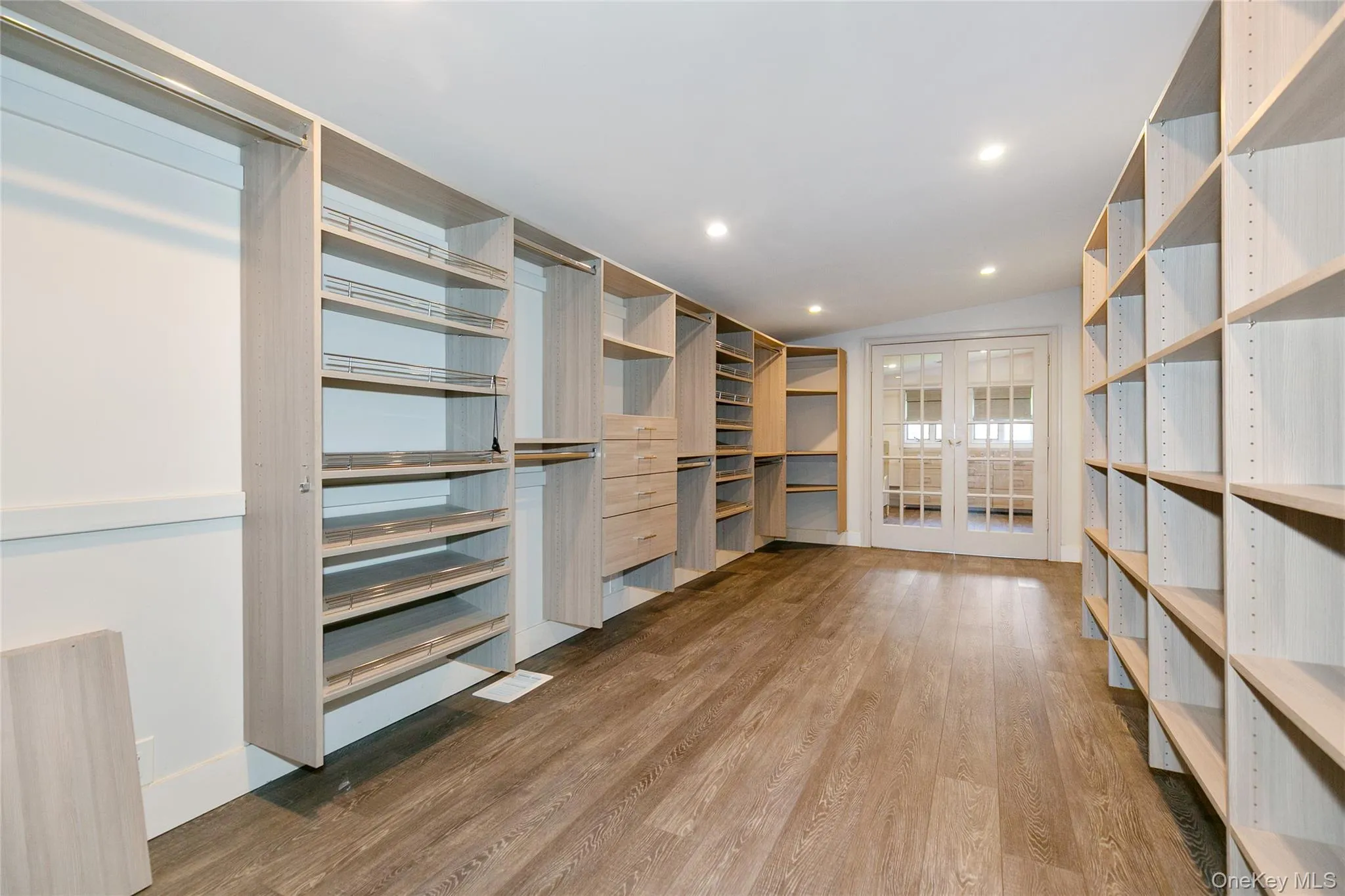Spacious closet featuring light wood finished floors, lofted ceiling, and french doors Spacious closet featuring light wood finished floors, lofted ceiling, and french doors