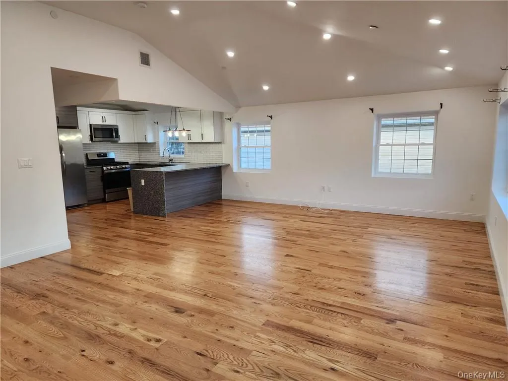 Kitchen with open floor plan, appliances with stainless steel finishes, vaulted ceiling, backsplash, and light wood-type flooring Kitchen with open floor plan, appliances with stainless steel finishes, vaulted ceiling, backsplash, and light wood-type flooring