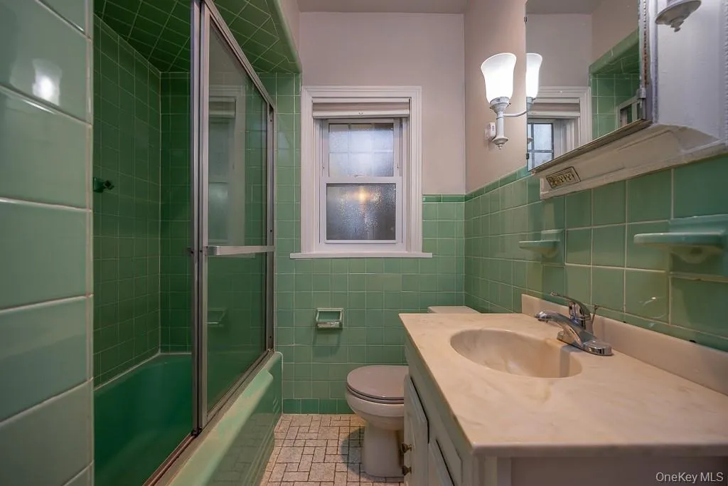 Full bath featuring vanity, tile walls, combined bath / shower with glass door, tile patterned flooring, and healthy amount of natural light Full bath featuring vanity, tile walls, combined bath / shower with glass door, tile patterned flooring, and healthy amount of natural light