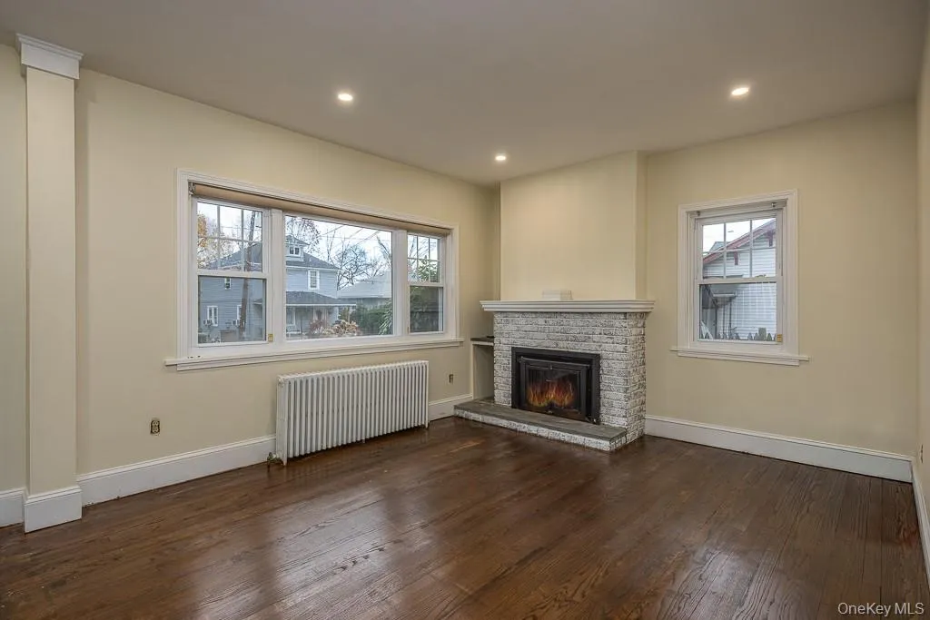 Unfurnished living room featuring radiator, dark wood finished floors, a brick fireplace, and recessed lighting Unfurnished living room featuring radiator, dark wood finished floors, a brick fireplace, and recessed lighting