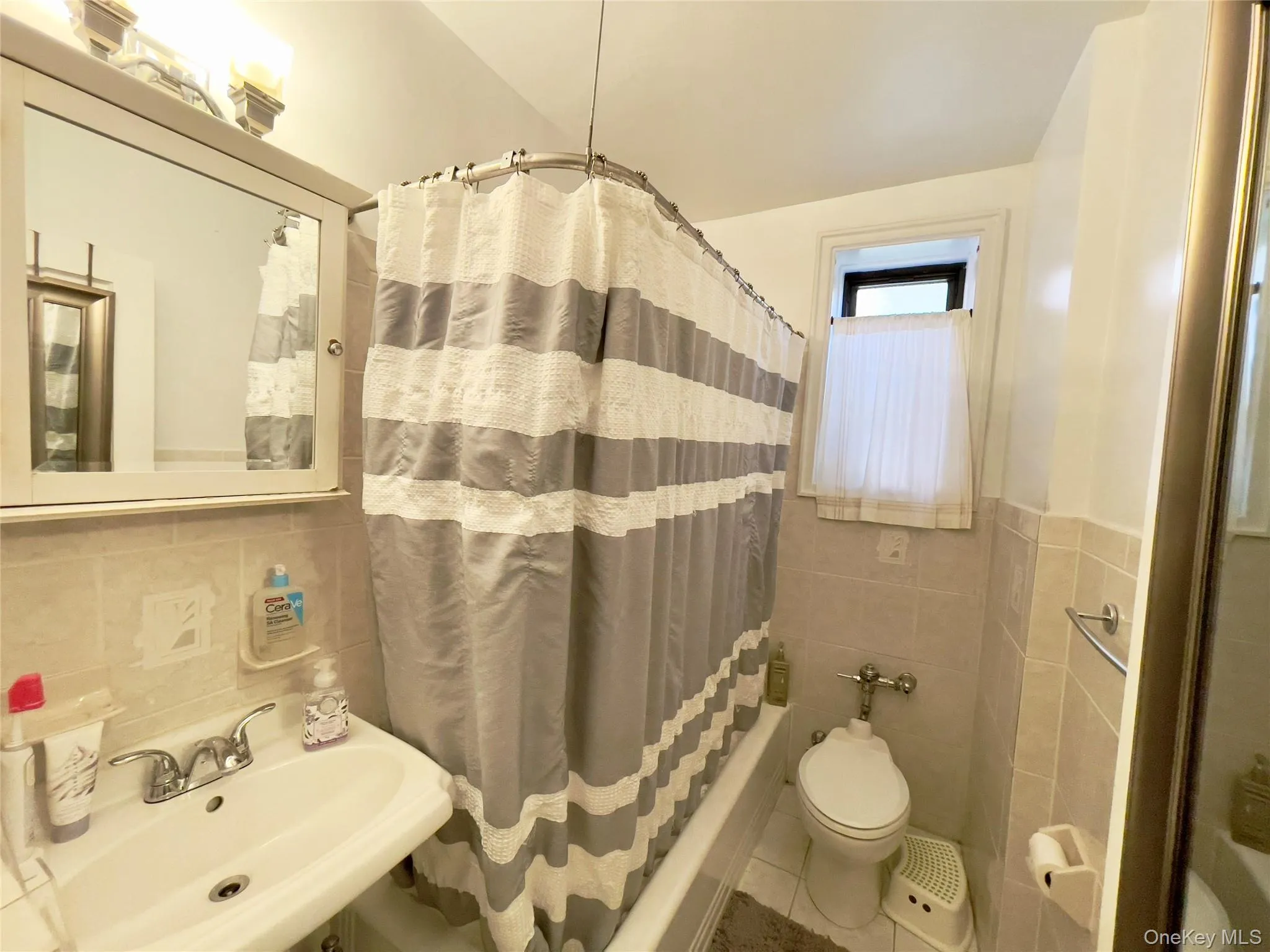 Full bathroom with tile walls, shower / bath combo, tile patterned flooring, and a wainscoted wall Full bathroom with tile walls, shower / bath combo, tile patterned flooring, and a wainscoted wall