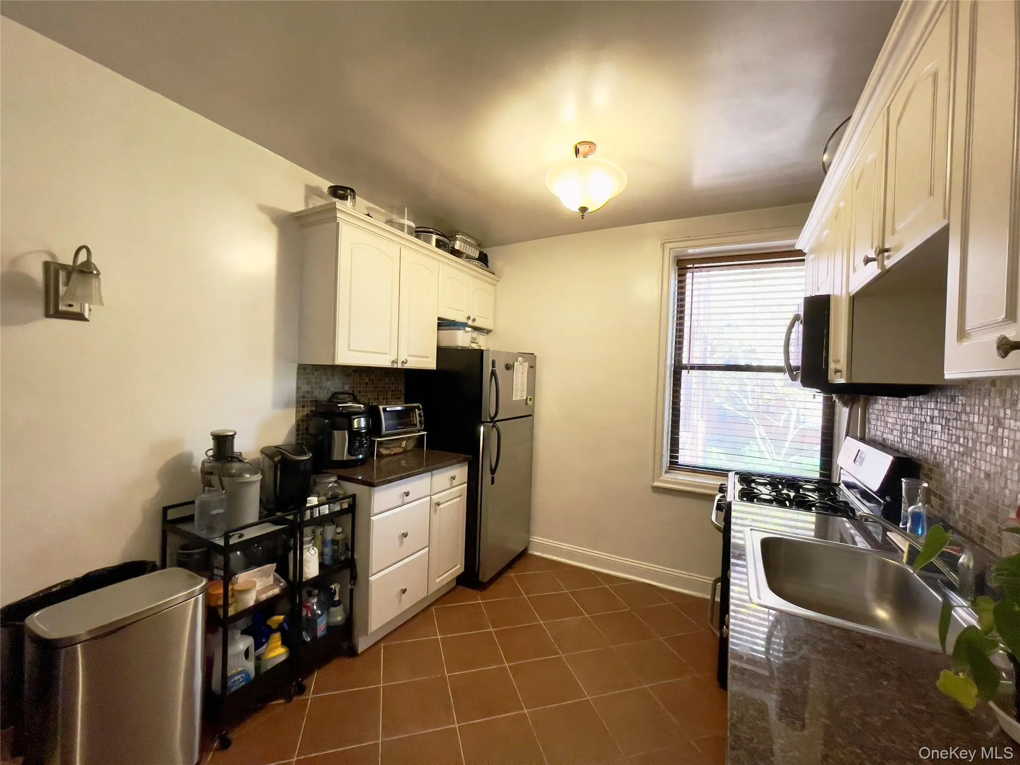 Kitchen featuring tasteful backsplash, dark tile patterned flooring, stainless steel appliances, white cabinets, and dark stone counters Kitchen featuring tasteful backsplash, dark tile patterned flooring, stainless steel appliances, white cabinets, and dark stone counters