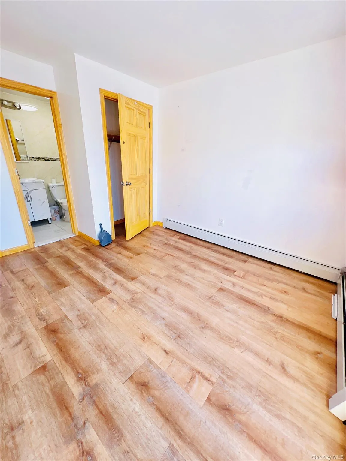 Unfurnished bedroom featuring light wood finished floors, a baseboard heating unit, a walk in closet, and ensuite bathroom Unfurnished bedroom featuring light wood finished floors, a baseboard heating unit, a walk in closet, and ensuite bathroom