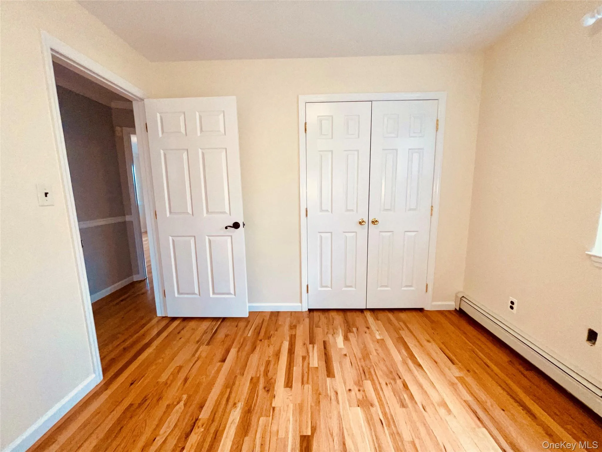 Unfurnished bedroom with a baseboard radiator, light wood finished floors, and a closet Unfurnished bedroom with a baseboard radiator, light wood finished floors, and a closet