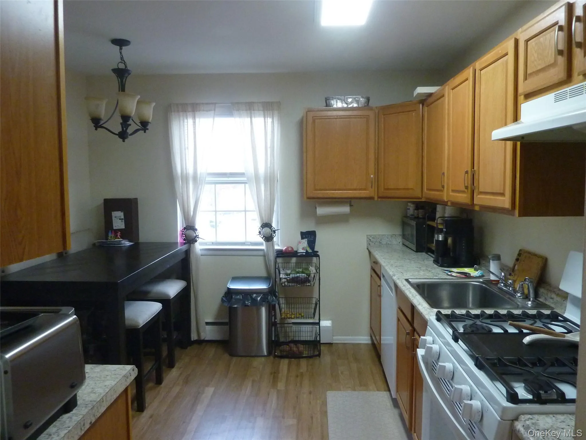 Kitchen featuring white appliances, light wood finished floors, light countertops, and decorative light fixtures Kitchen featuring white appliances, light wood finished floors, light countertops, and decorative light fixtures