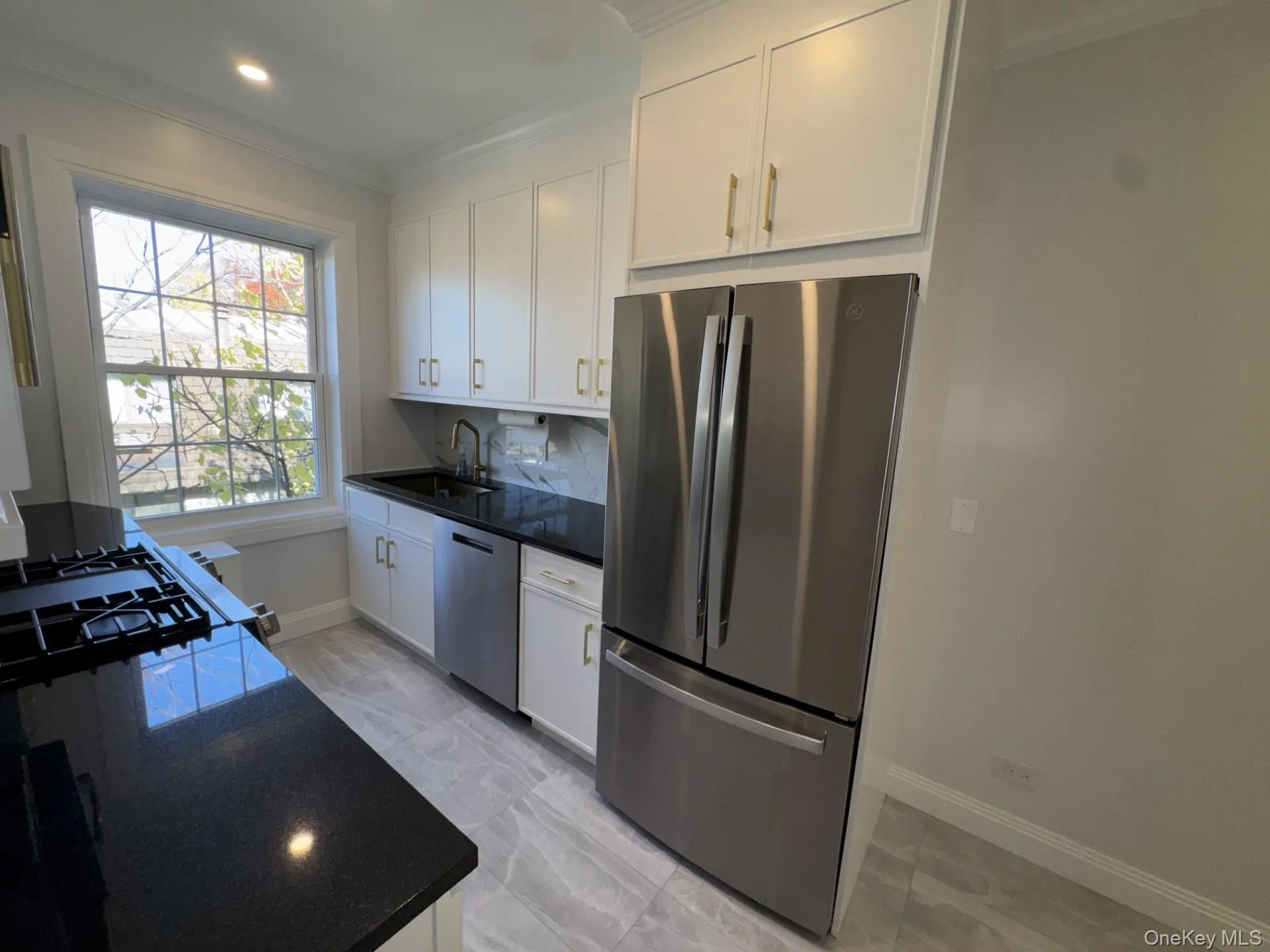 Kitchen with appliances with stainless steel finishes, ornamental molding, tasteful backsplash, dark stone countertops, and white cabinetry Kitchen with appliances with stainless steel finishes, ornamental molding, tasteful backsplash, dark stone countertops, and white cabinetry