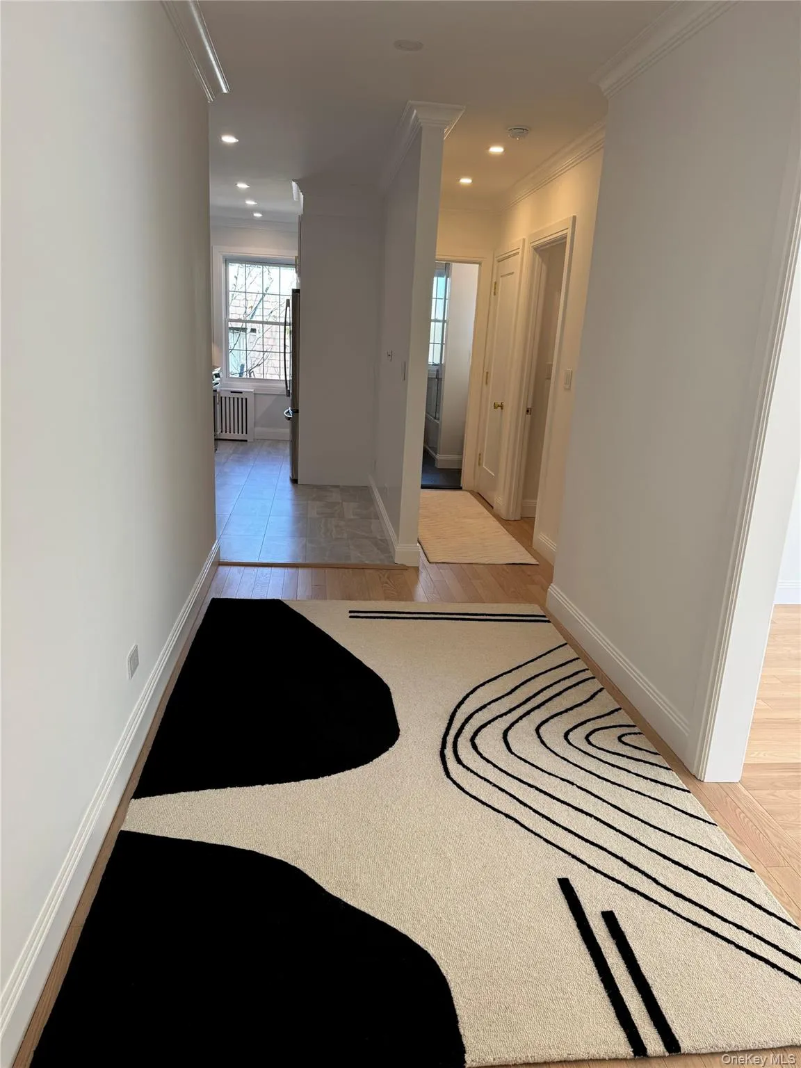 Corridor with crown molding, light wood-style flooring, recessed lighting, and radiator heating unit Corridor with crown molding, light wood-style flooring, recessed lighting, and radiator heating unit