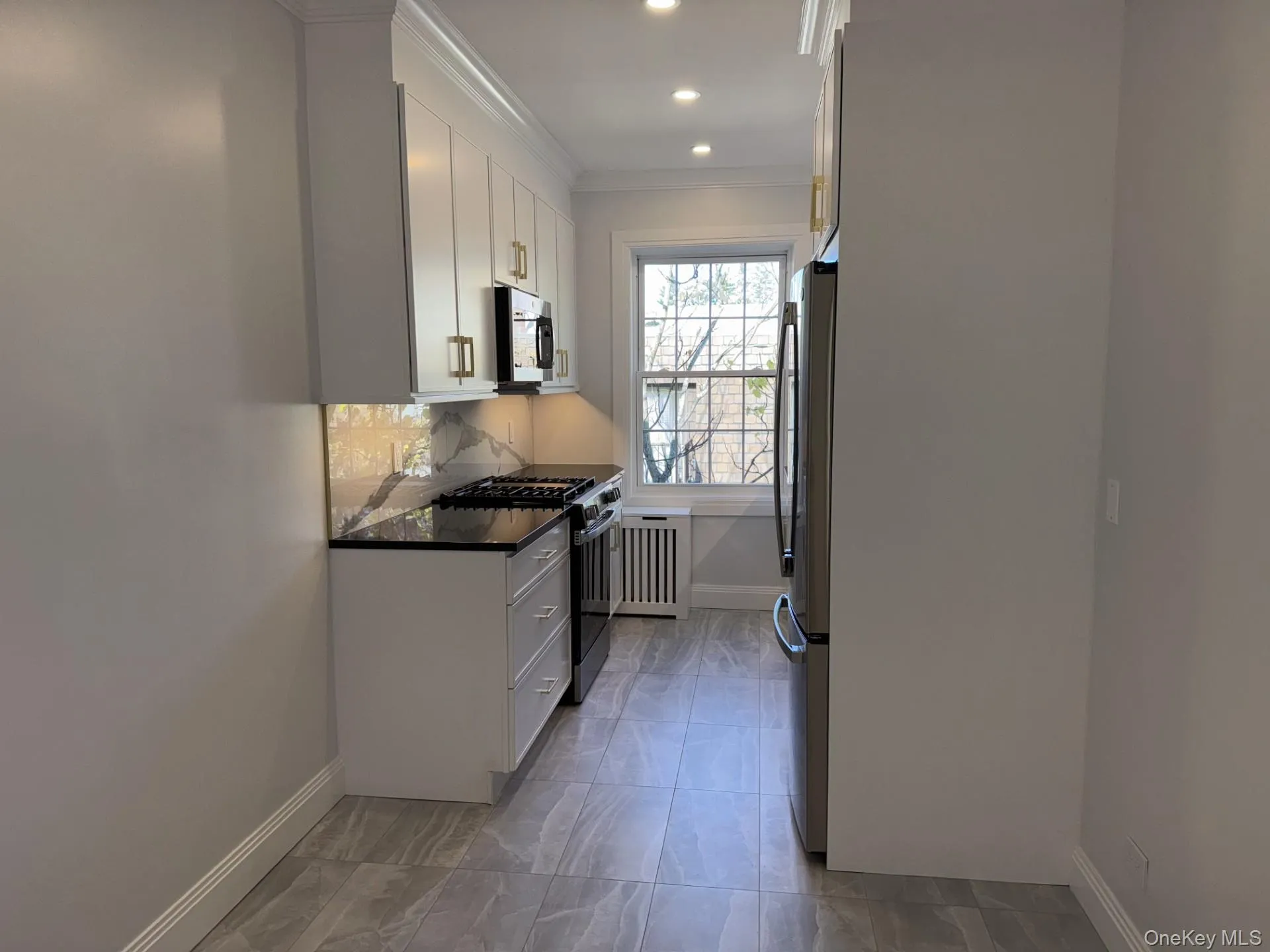 Kitchen featuring white cabinetry, appliances with stainless steel finishes, decorative backsplash, dark stone countertops, and crown molding Kitchen featuring white cabinetry, appliances with stainless steel finishes, decorative backsplash, dark stone countertops, and crown molding