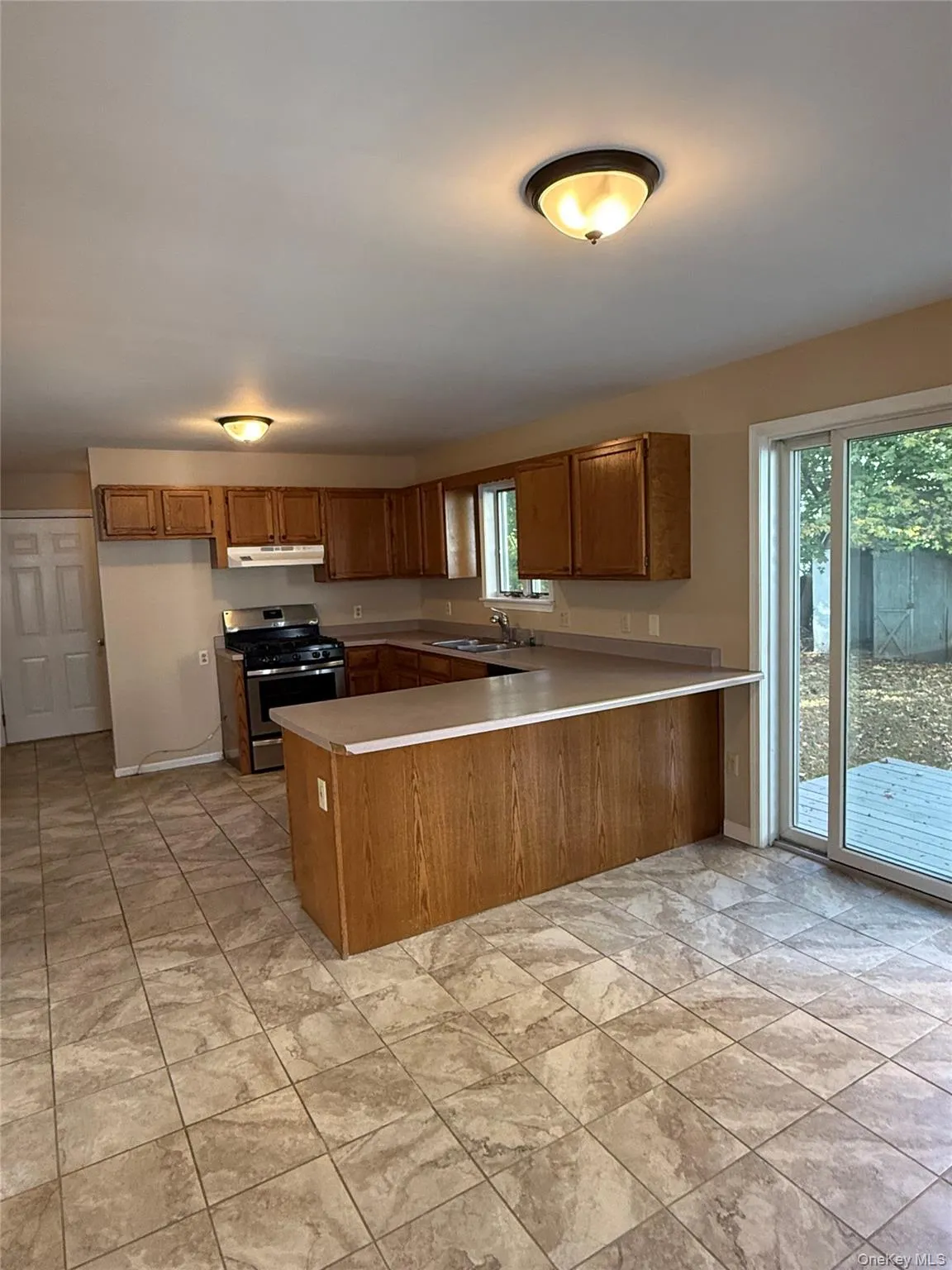 Kitchen featuring brown cabinets, stainless steel gas stove, a peninsula, and light countertops Kitchen featuring brown cabinets, stainless steel gas stove, a peninsula, and light countertops