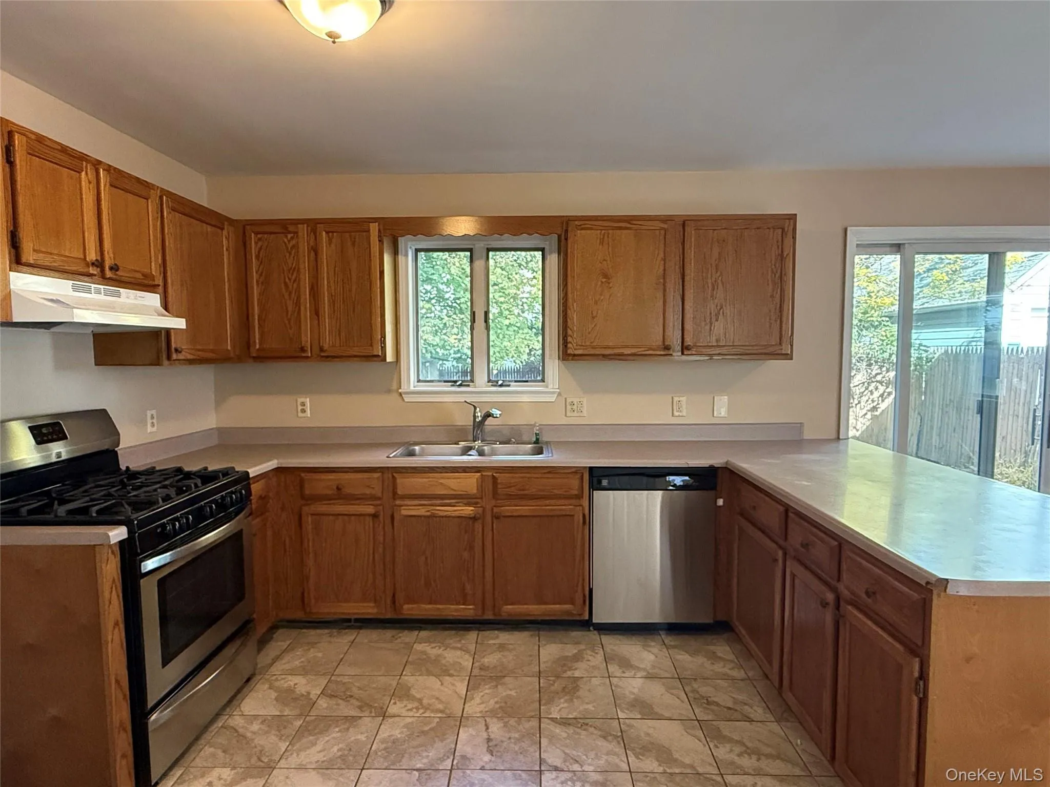 Kitchen with stainless steel appliances, a peninsula, brown cabinets, and under cabinet range hood Kitchen with stainless steel appliances, a peninsula, brown cabinets, and under cabinet range hood