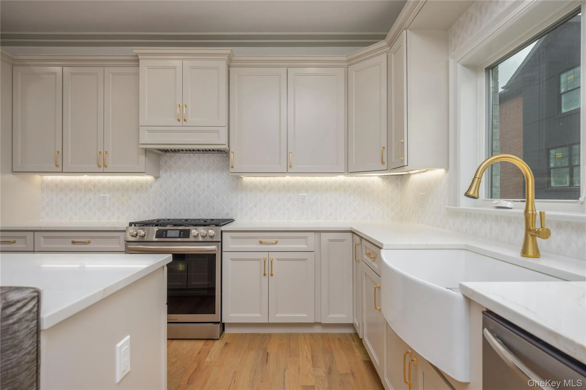 Kitchen with stainless steel appliances, light stone counters, light wood-style flooring, backsplash, and under cabinet range hood Kitchen with stainless steel appliances, light stone counters, light wood-style flooring, backsplash, and under cabinet range hood