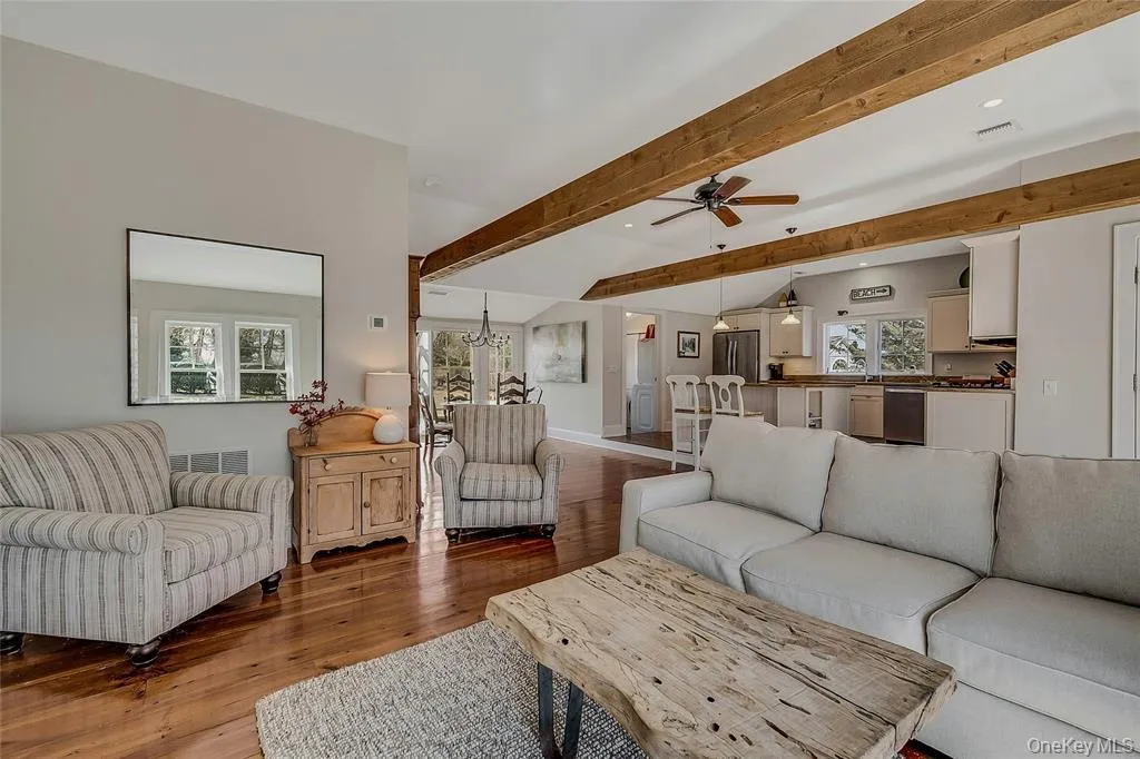 Living area featuring beamed ceiling, wood floors, and a ceiling fan Living area featuring beamed ceiling, wood floors, and a ceiling fan