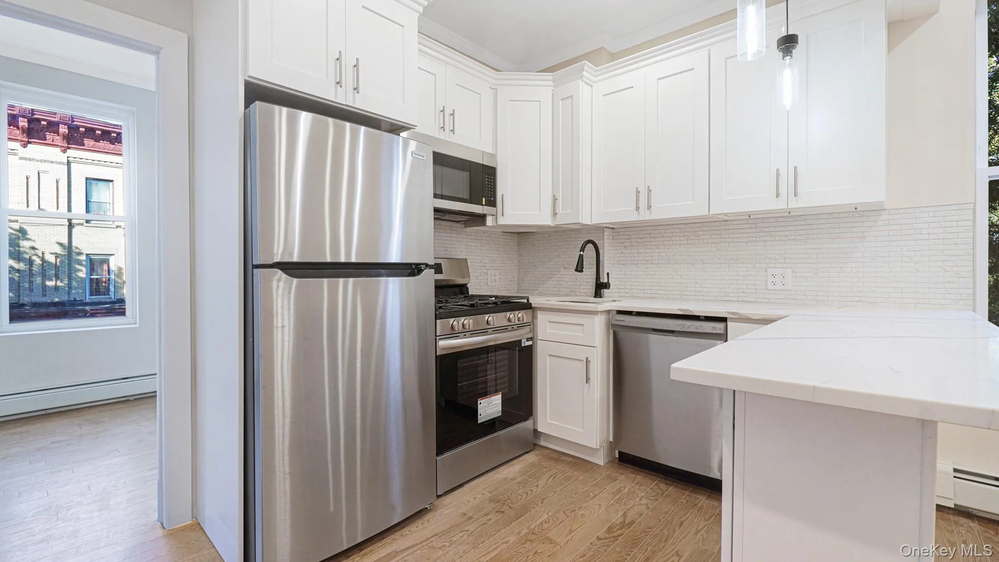 Kitchen with stainless steel appliances, decorative backsplash, light wood finished floors, white cabinetry, and a peninsula Kitchen with stainless steel appliances, decorative backsplash, light wood finished floors, white cabinetry, and a peninsula
