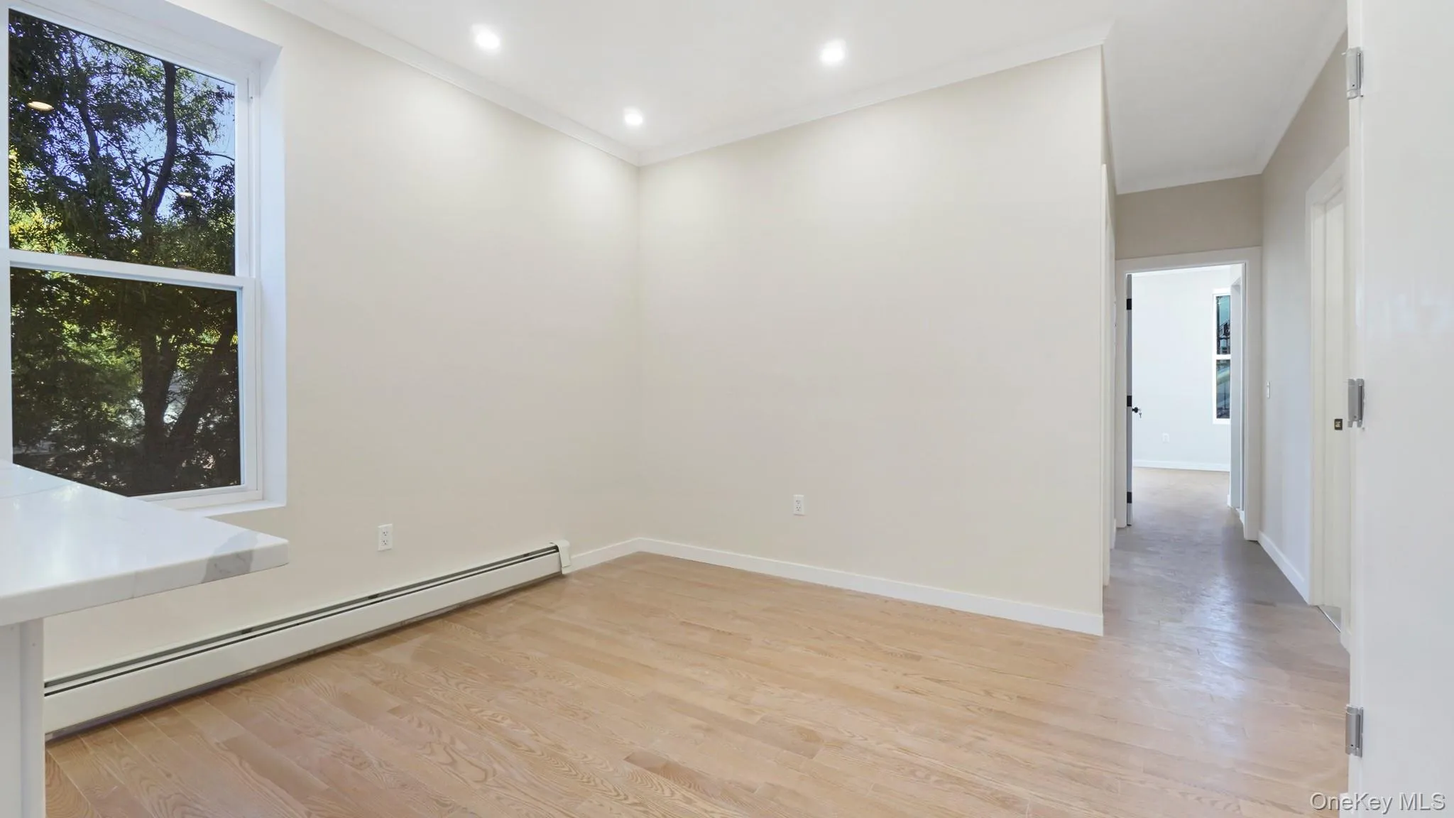 Empty room with a baseboard radiator, light wood finished floors, crown molding, and recessed lighting Empty room with a baseboard radiator, light wood finished floors, crown molding, and recessed lighting