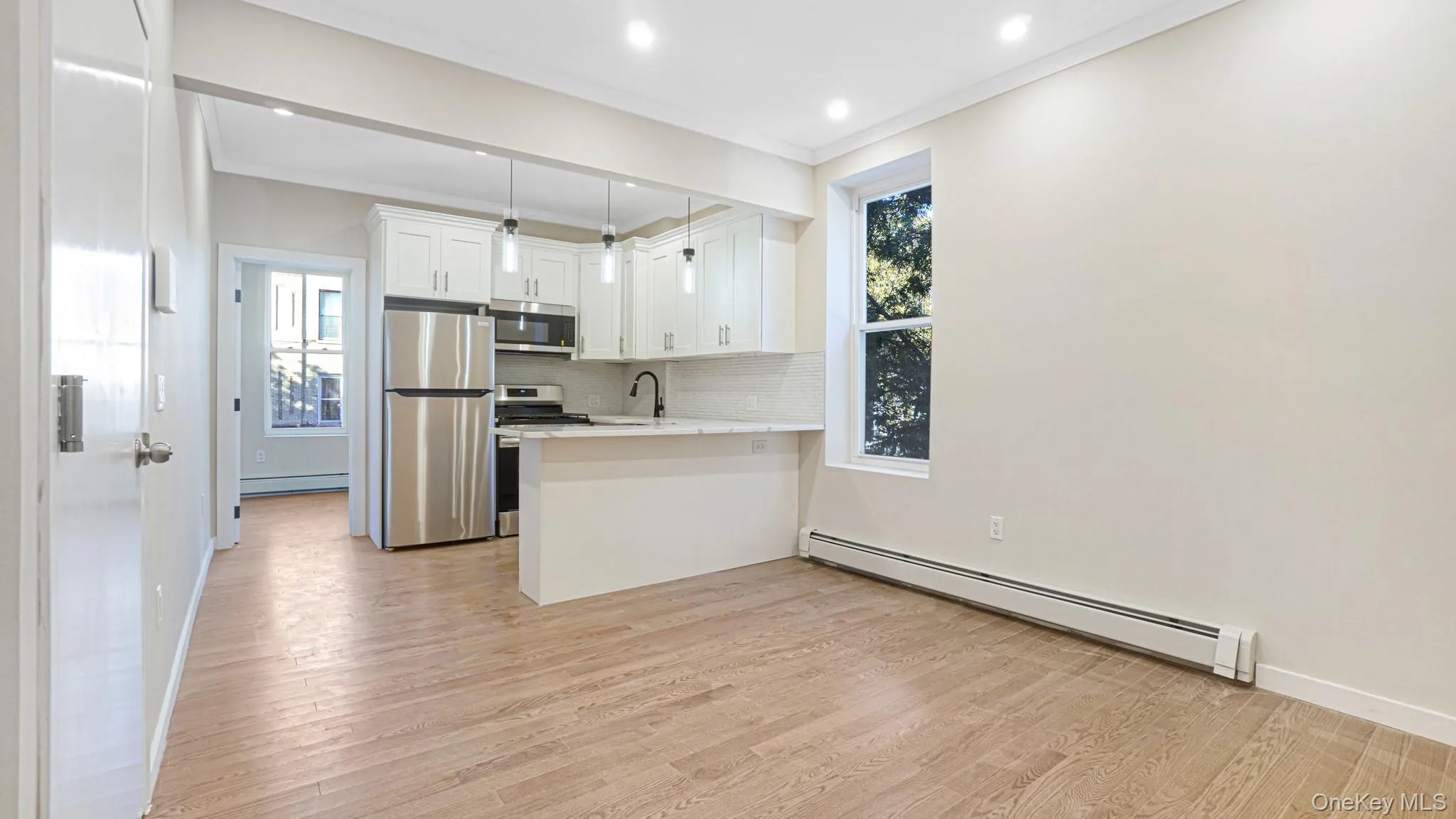 Kitchen featuring white cabinetry, a baseboard radiator, stainless steel appliances, light wood-type flooring, and decorative backsplash Kitchen featuring white cabinetry, a baseboard radiator, stainless steel appliances, light wood-type flooring, and decorative backsplash