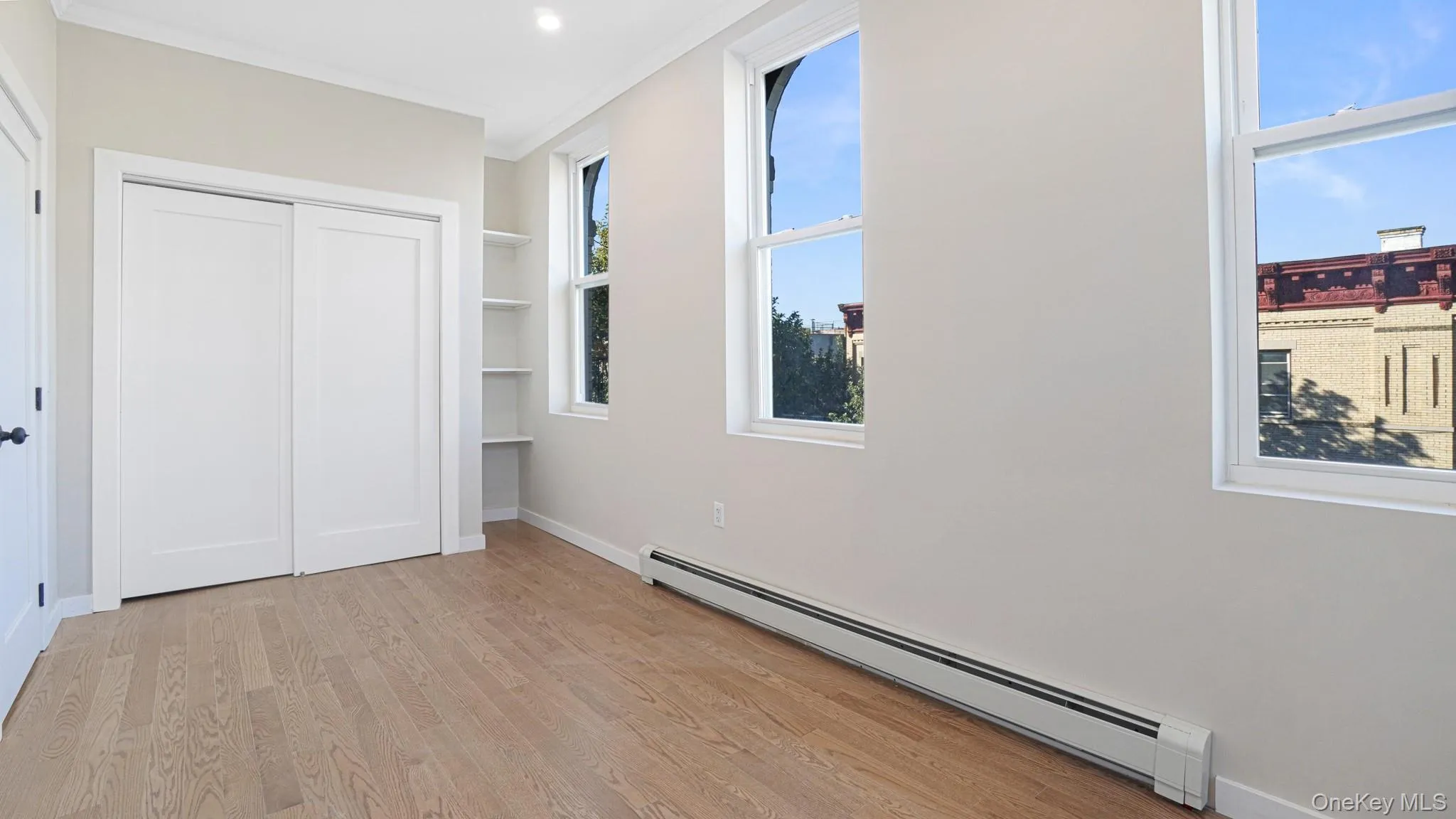 Unfurnished bedroom with a baseboard heating unit, light wood finished floors, crown molding, and a closet Unfurnished bedroom with a baseboard heating unit, light wood finished floors, crown molding, and a closet