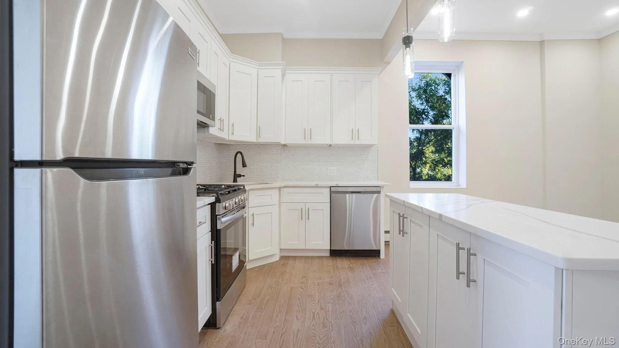 Kitchen with appliances with stainless steel finishes, tasteful backsplash, white cabinetry, light wood-style flooring, and ornamental molding Kitchen with appliances with stainless steel finishes, tasteful backsplash, white cabinetry, light wood-style flooring, and ornamental molding