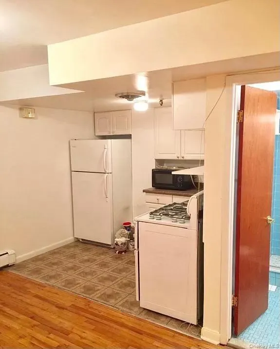 Kitchen featuring white cabinets, white appliances, light wood-type flooring, and a baseboard heating unit Kitchen featuring white cabinets, white appliances, light wood-type flooring, and a baseboard heating unit