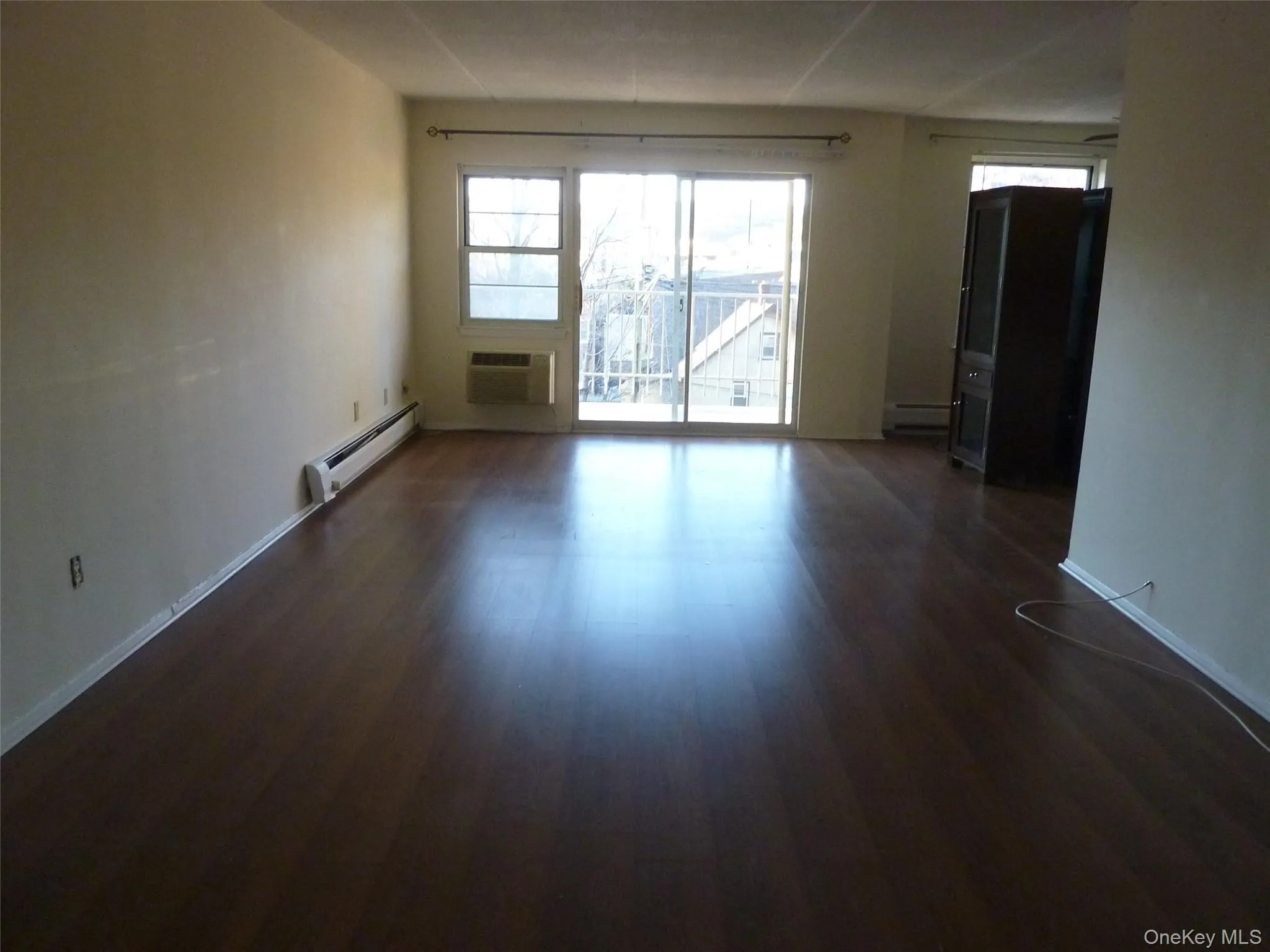 Spare room with baseboard heating, dark wood-type flooring, and a wall mounted air conditioner Spare room with baseboard heating, dark wood-type flooring, and a wall mounted air conditioner